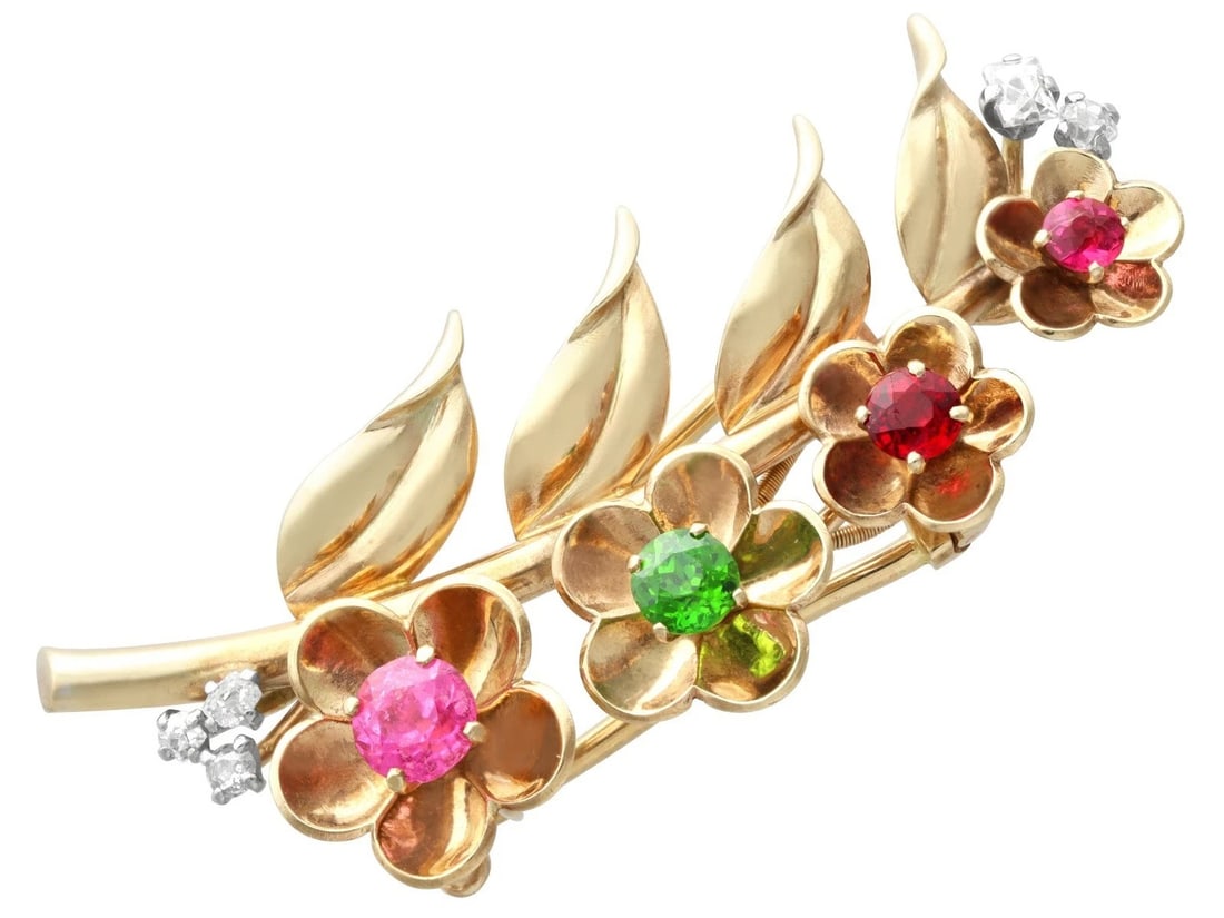 GOLD-TONE MULTICOLOR FLORAL BROOCH: GOLD-TONE MULTICOLOR FLORAL BROOCH Description: A floral spray brooch in gold-tone metal, composed of clustered red, green, pink, and colorless stones arranged as blossoms and leaves on branching stem