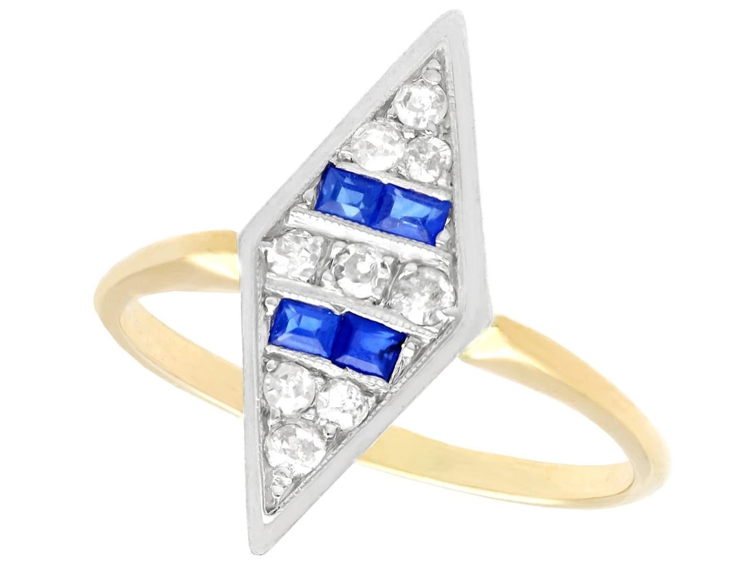 GOLD-TONE BLUE AND COLORLESS STONE BYPASS RING: GOLD-TONE BLUE AND COLORLESS STONE BYPASS RING Description: A slender gold-tone bypass ring with opposing geometric terminals, one set with a deep-blue stone and the other with a colorless stone, acce