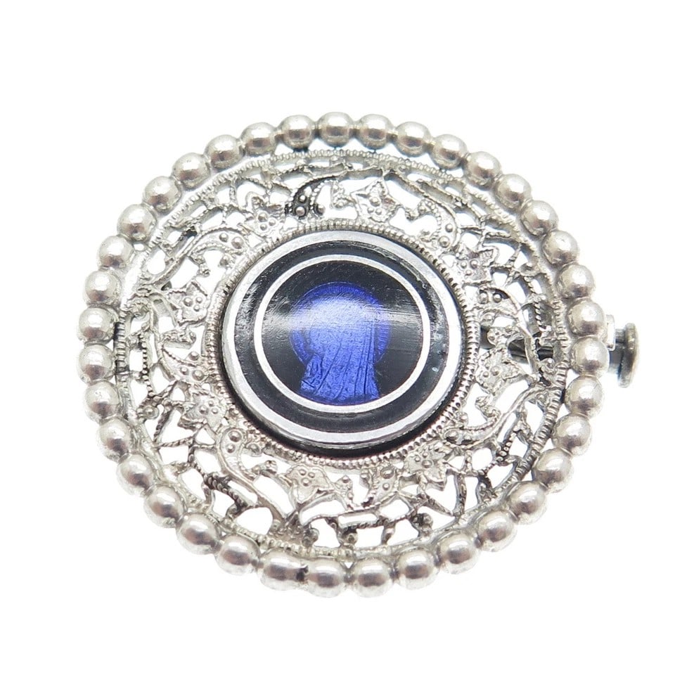 VINTAGE SILVER-TONE FILIGREE BROOCH WITH BLUE GLASS MEDALLION: VINTAGE SILVER-TONE FILIGREE BROOCH WITH BLUE GLASS MEDALLION Description: The brooch is designed in a circular format with an outer border composed of evenly spaced raised bead-like elements framing 