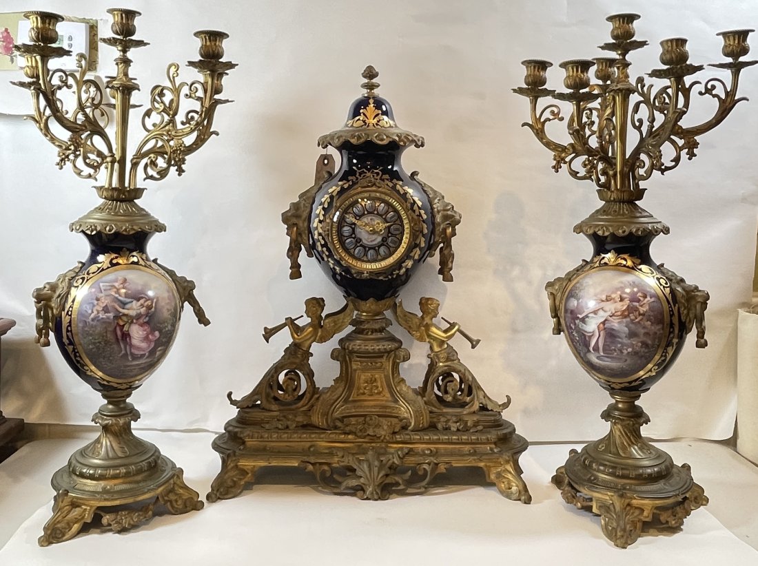 19th Century 3 Piece Sevres Bronze & Porceain Clock Set: Large clock with winged nude women holding trumpets on the sides, large lion masks on side. Hand painted scenic dial, with mathing candelabras. Overall very good condition, the back door of the clock 