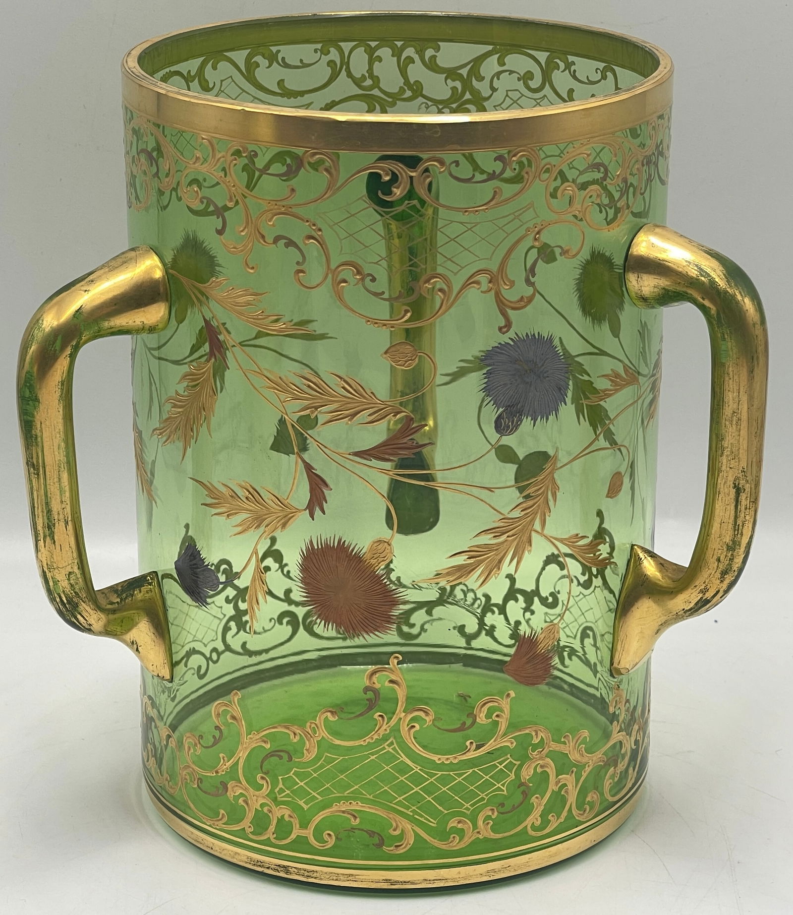 Moser Gilt Trimmed Loving Cup: Three handled green Moser glass cup with gilt trim and flowers adoring glass. No chips or cracks. 7 in tall, 4.75 in diameter across opening.