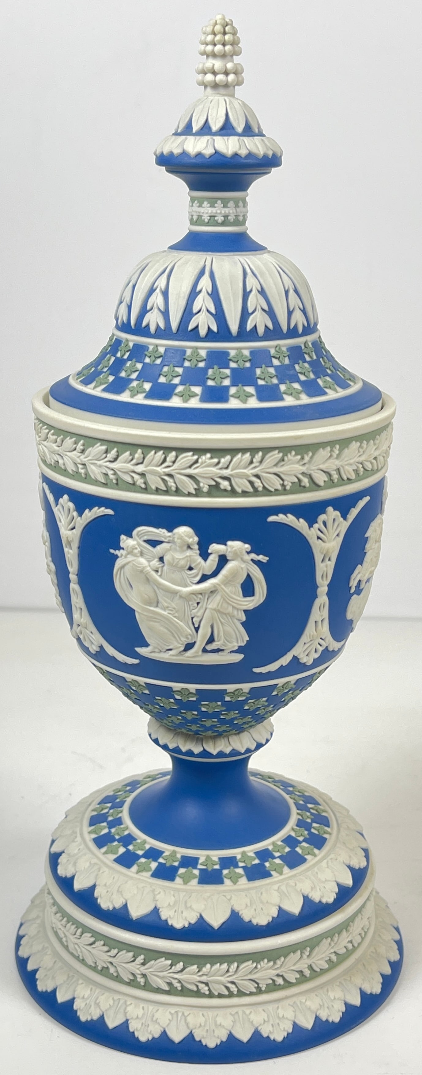 Wedgwood Jasperware Dip Diceware Covered Vase: Urn-shaped vase in dark blue Jasperware dip with sage green quatrefoils and white foliate and foliage borders. Depicts in white raised reliefs: Cupid As Oracle, Three Graces, Aurora, and Nike And The