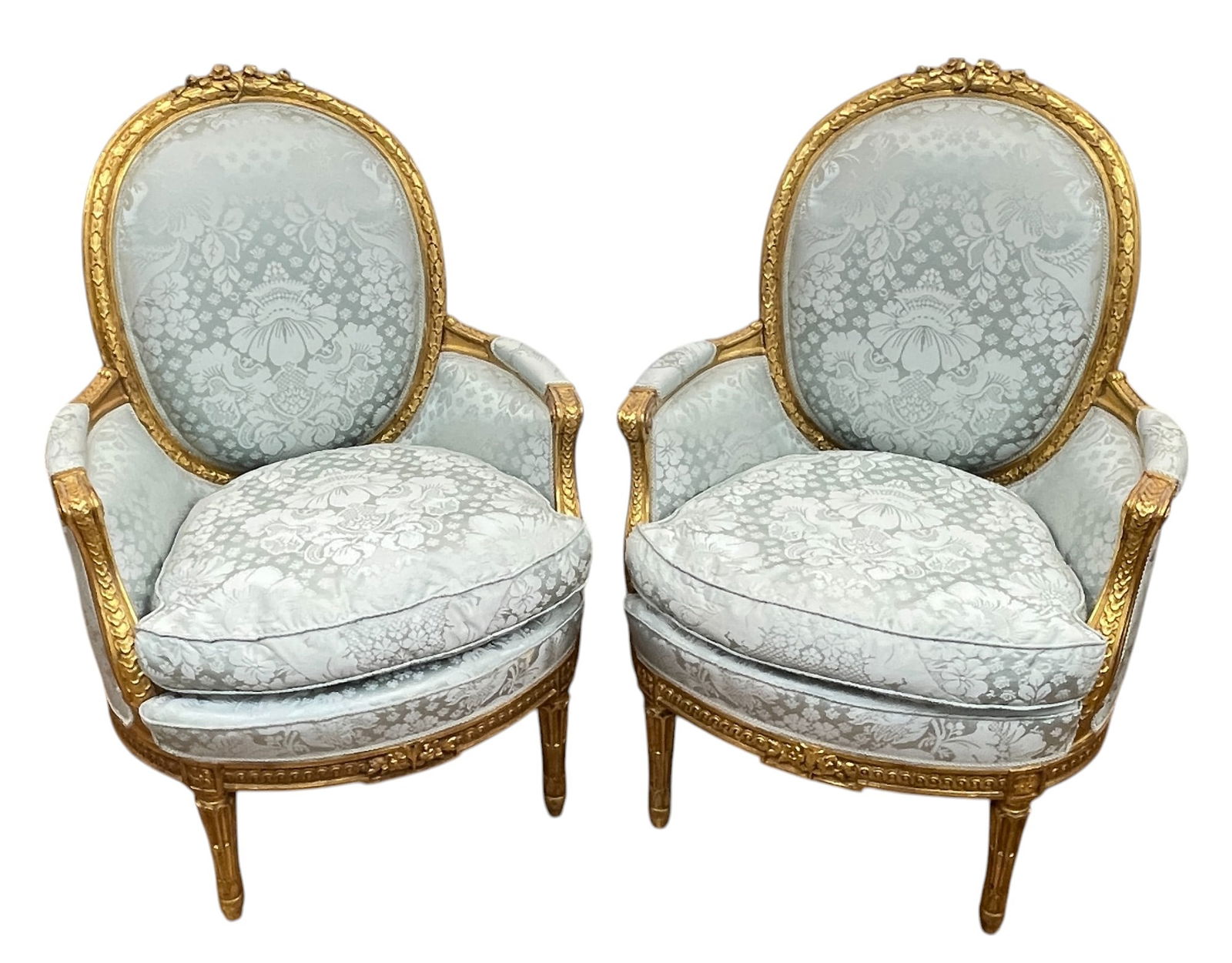 Pair Louis XVI Carved Gilt Wood Silk Upholstered Bergere Chairs: Overall carved, floral carved at the top. Beautiful blue silk lampas upholstry. Overall very good condition. Measure 41 inches high, 27 inches wide, 27 inches deep.