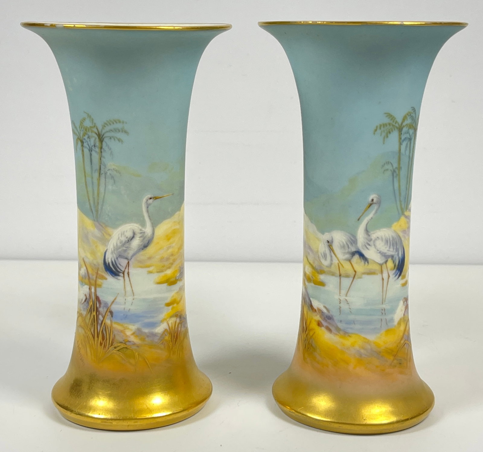 Pair Royal Worcester Stork Vases by George Johnson: Both with wading storks by a tropical shore. Signed G Johnson. Vases measure just shy of 6 inches high, 3.125 inches across the top. Overall fair condition, one chip around the bottom of one rim that 