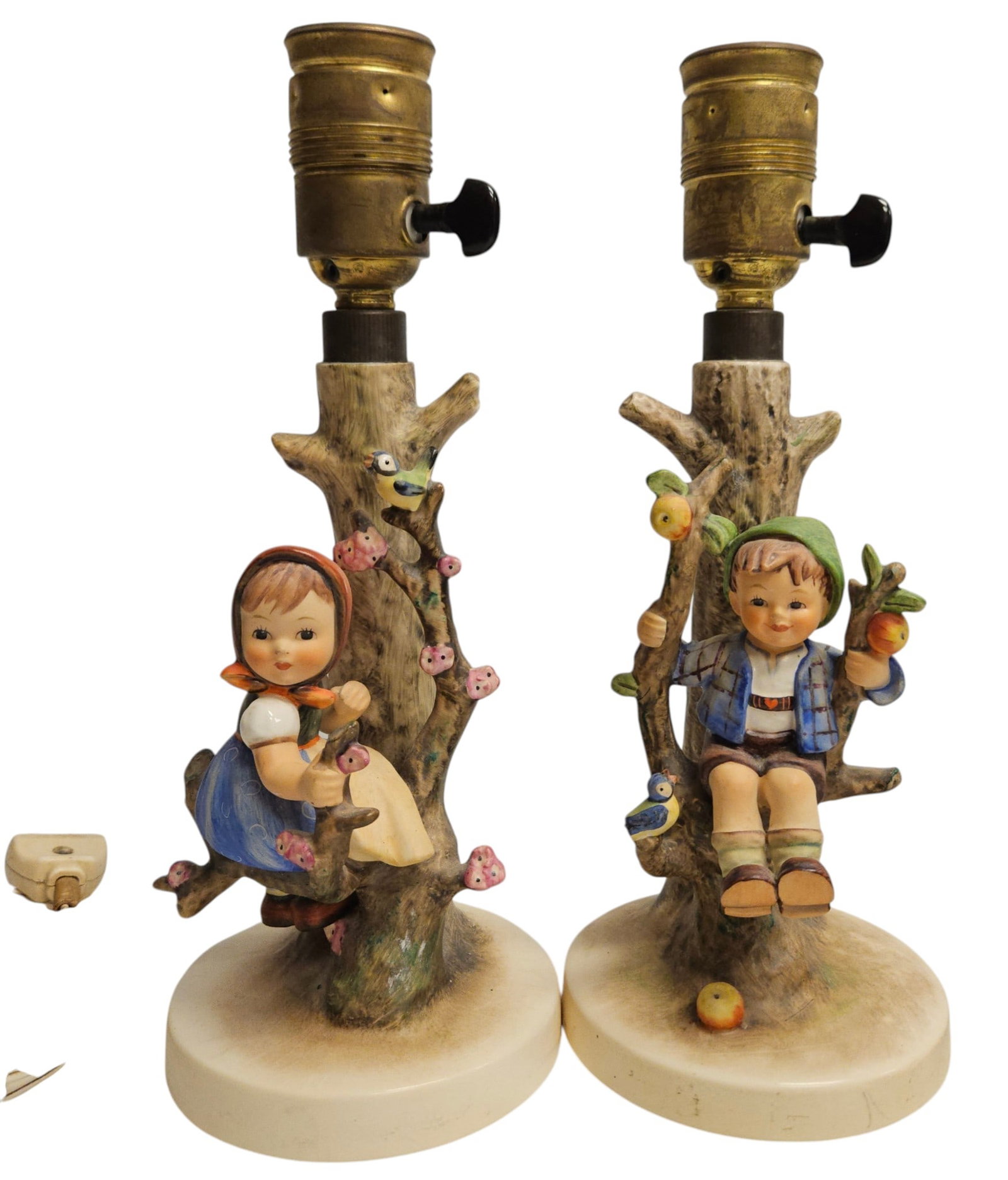 Pair Hummel Table Lamps: German Hummel table lamps. Boy in apple tree with bird (230), tip of tail missing, and apple tree girl (229). Mark is 1960-1972. 10.75 inches high to top of socket. Overall good condition.