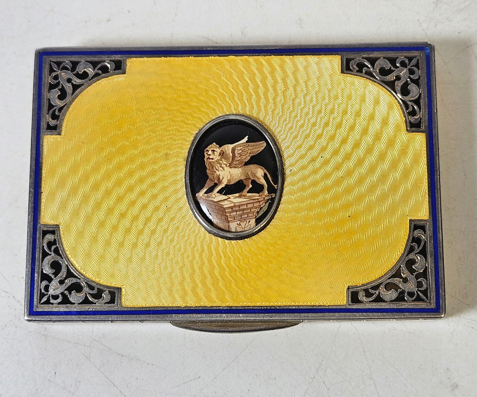Italian Art Deco Silver & Two Tone Enamel Cigarette Case: Featuring blue enamel border, reticulated corners, and a yellow enamel ground with a central winged lion in the center. Measures 3.5 inches x 2.5 inches. Overall good condition, had damage and was