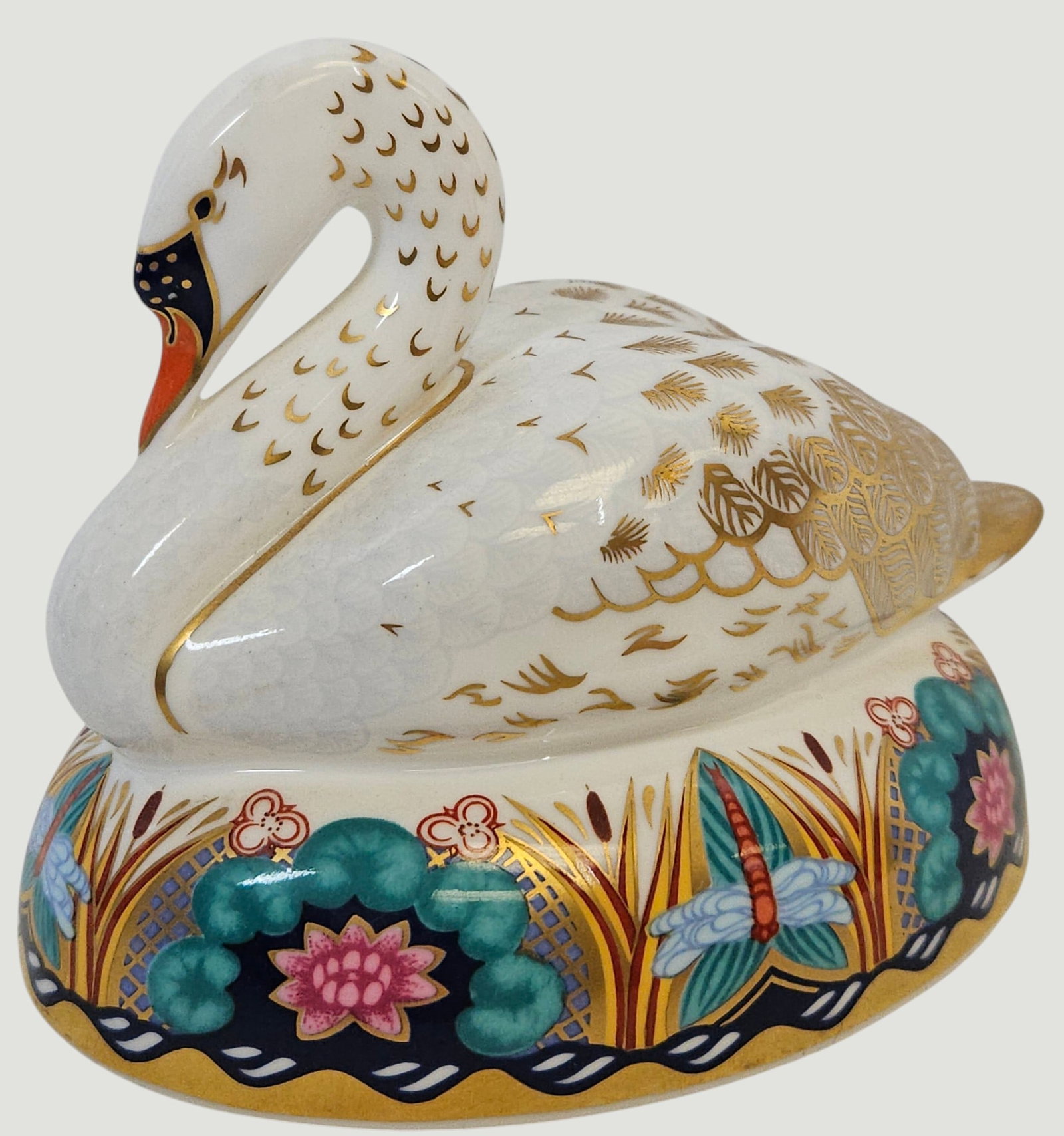 Royal Crown Derby Porcelain White Swan: A Royal Crown Derby English bone china paperweight modeled as a swan that features a white glaze with gilt-highlighted plumage. The base is decorated with a pattern of dragonflies and water lilies in