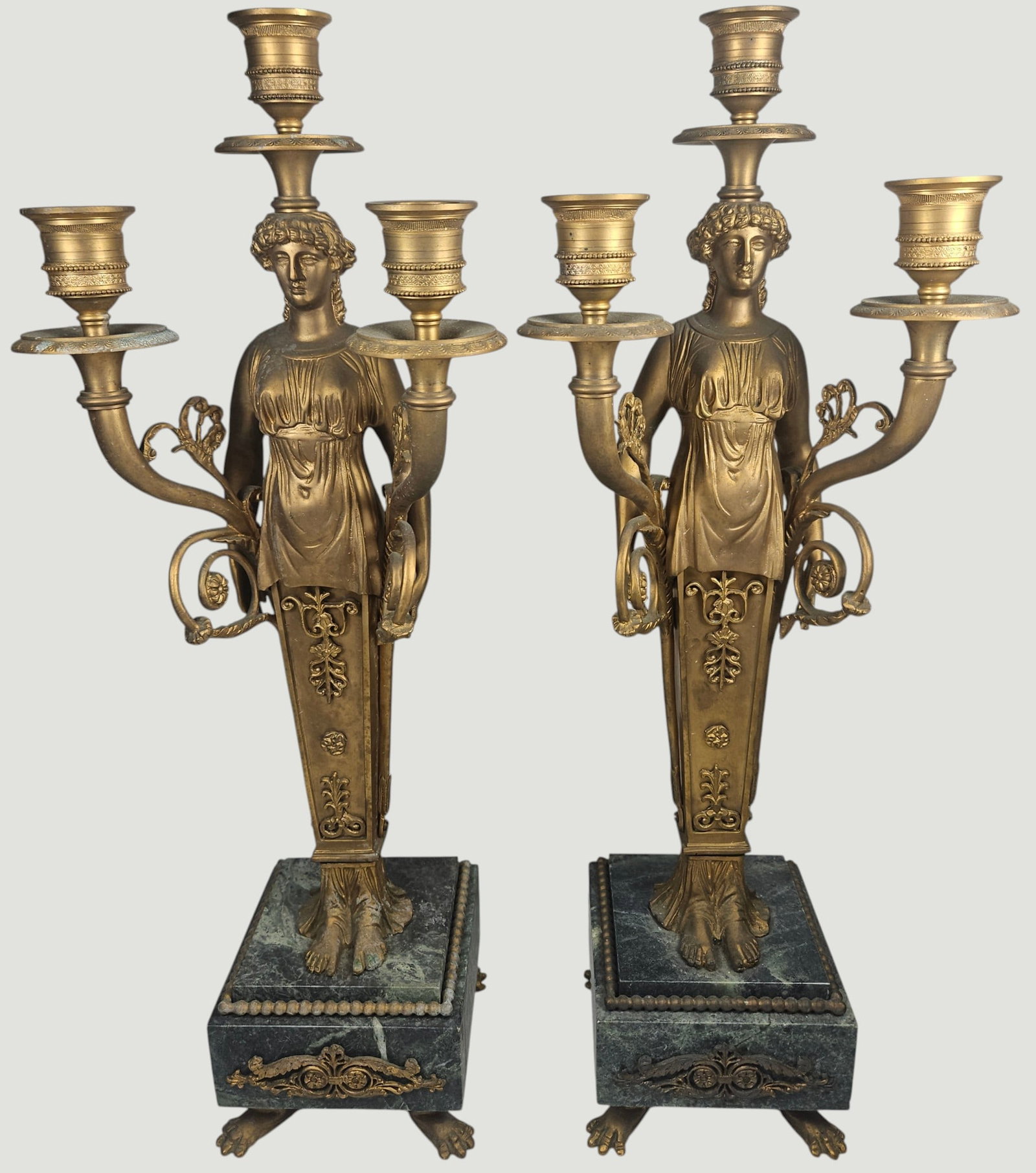 Pair 19th Century French Empire Figural Gilt Bronze Candelabras: Toga clad female figure standing ona green marble pedestal base, with scrolled arms extending to hold the candlesticks. Measure 17.75 inches high, 4.125 square base. Overall good condition, some disco