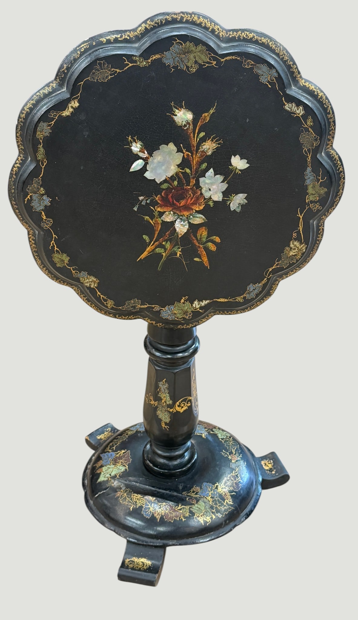 19th Century Papier Mache Mother of Pearl Tilt Top Table: Antique 19th-century black lacquered pedestal table with scalloped oval top, hand-painted gilt accents, and iridescent mother-of-pearl floral inlay. Measures 35 inches tilted,19 inches in diameter.