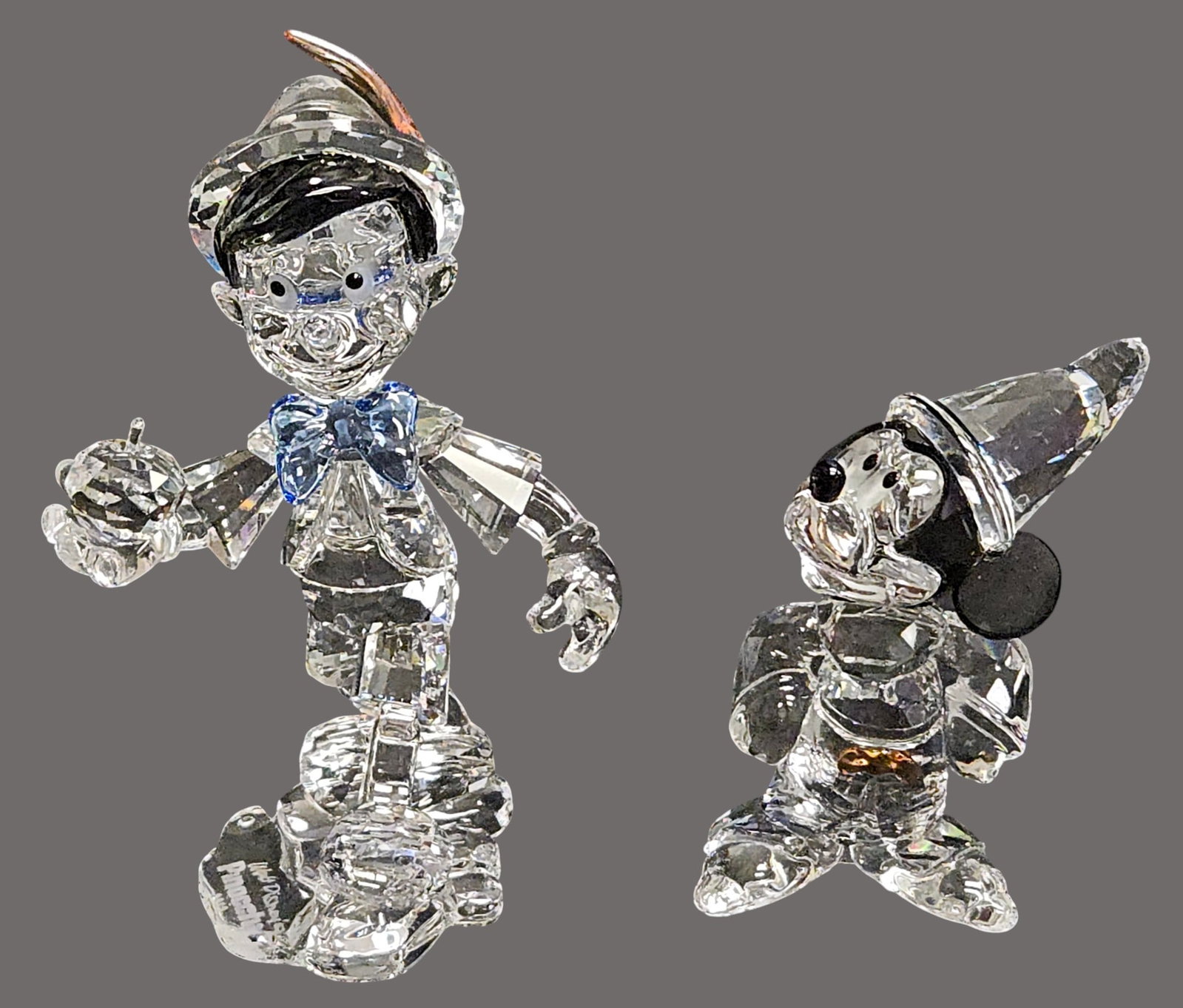 (2) Swarovski Crystal Disney Sorcerer Mickey & Pinocchio: To include Crystal Mickey who looks like a magician with head and ears in Black Diamond crystal and his Jet crystal nose add the gleam of a wizard. A Topaz crystal bow glows at the waist. The seam of