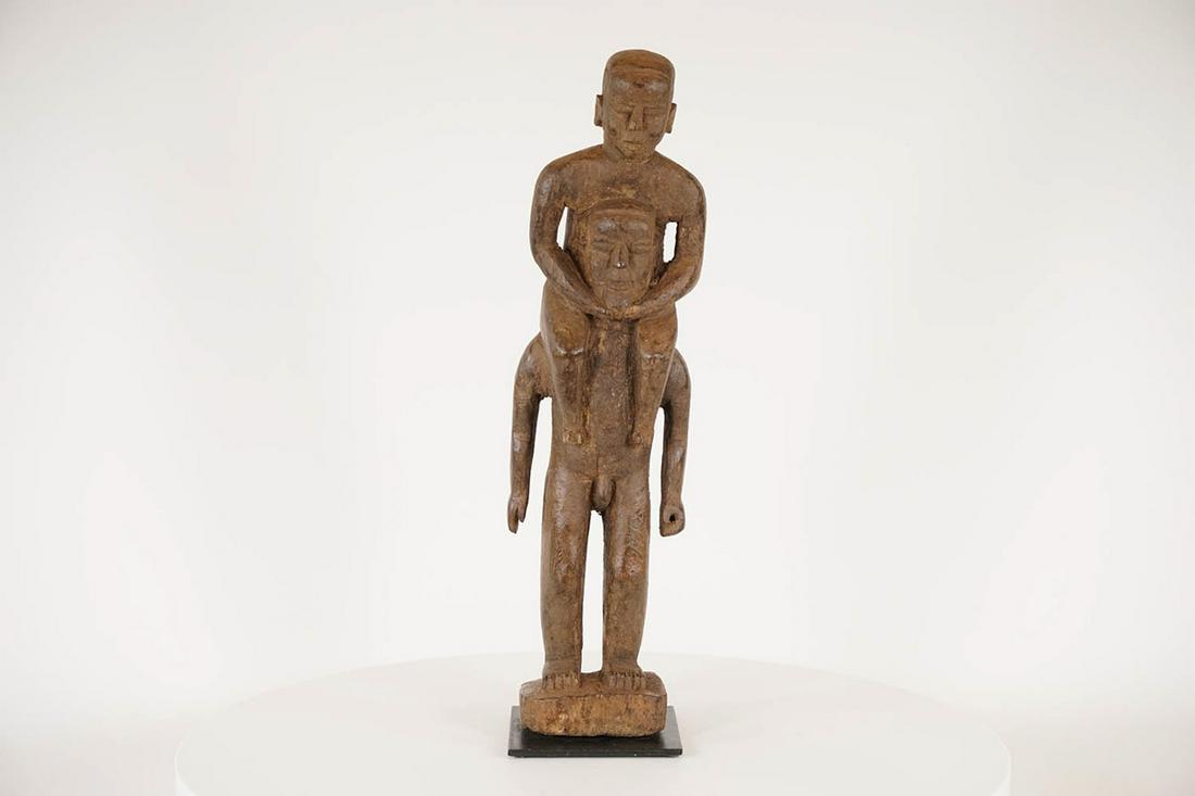 Nigerian Figure - African Tribal Art Sculpture: Measurements (inches) & Weight (pounds) Height: 19.75" Width: 5.5" Depth: 4" Weight: 4 lbs A figure featuring a standing male figure with another figure riding on his shoulders, secured to a metal