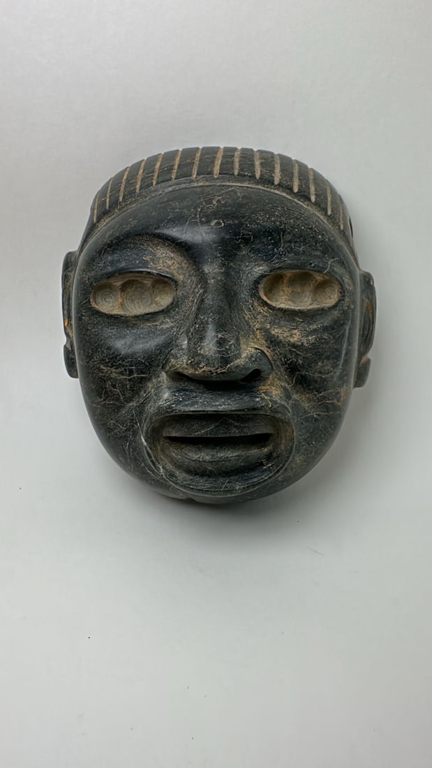 PRE-COLUMBIAN AZTEC SERPENTINE XIPE TOTEC PECTORAL MASK: PRE-COLUMBIAN AZTEC SERPENTINE XIPE TOTEC PECTORAL MASKStriking Aztec serpentine pectoral mask depicting Xipe Totec, the powerful deity associated with renewal, rebirth, agriculture, and ritual transf
