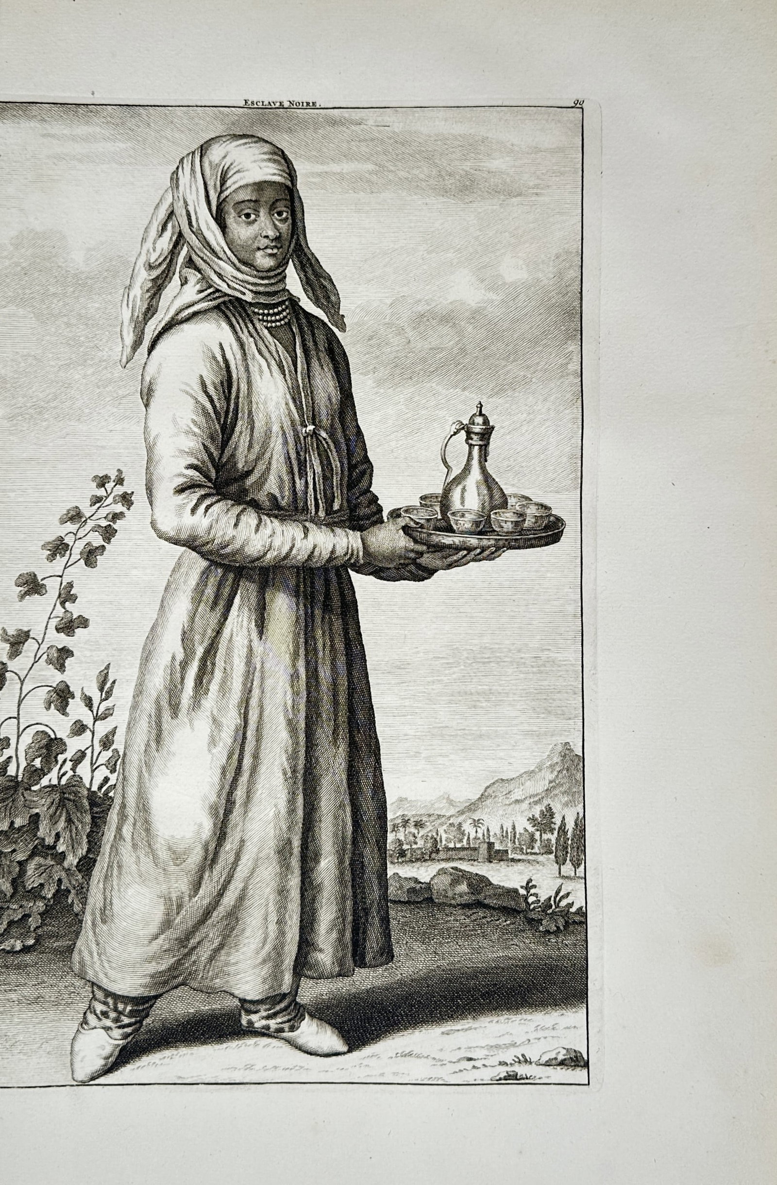 Cornelis de Bruijn – Esclave Noire Carrying a Serving Tray – Engraving (1714): "Esclave Noire" features a full-length ethnographic portrait of a figure wearing a headscarf, a necklace, and traditional long robes while holding a circular serving tray arranged with a decorative ew