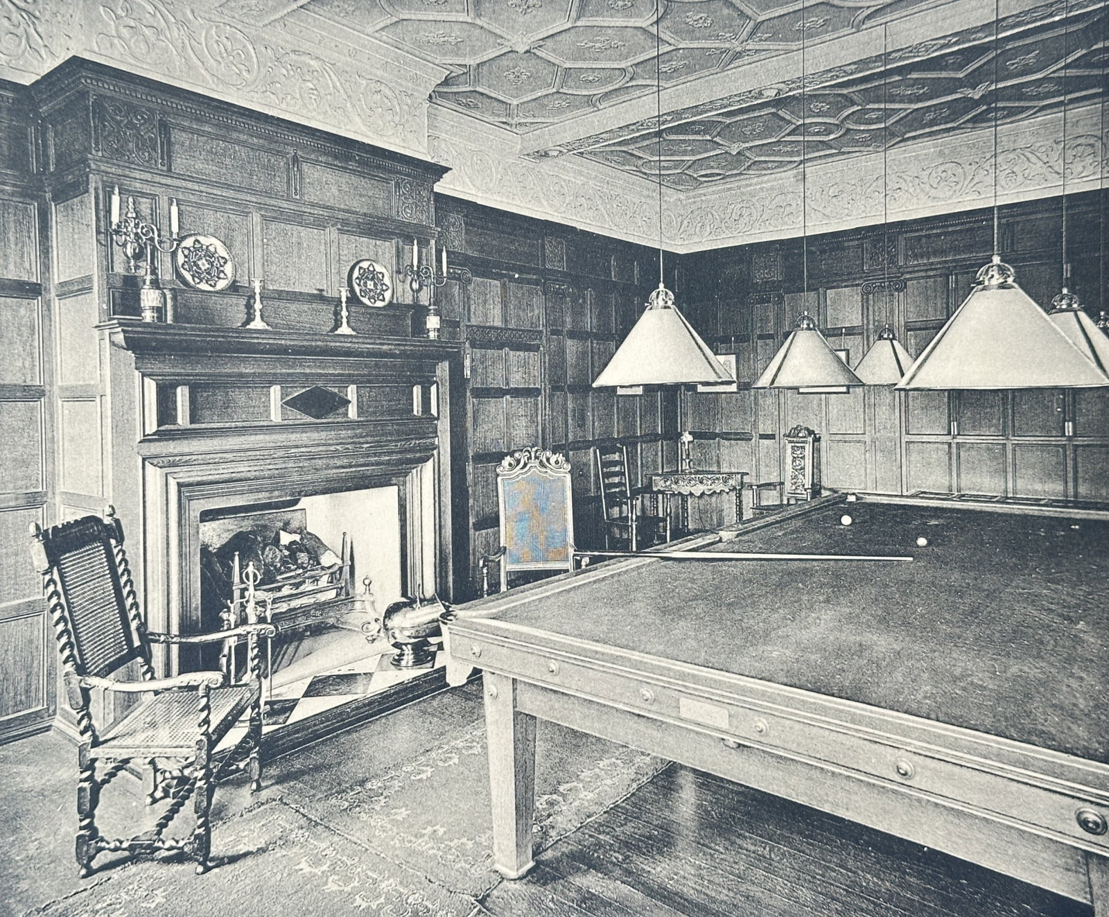 Louis Antonio Hayes – Salon at Fernhurst Country House – Collotype (1910): "The English Interior" This print features a wide view of a spacious Edwardian living room adorned with intricate floral upholstery, a classical fireplace, and indoor palm trees. The view is published