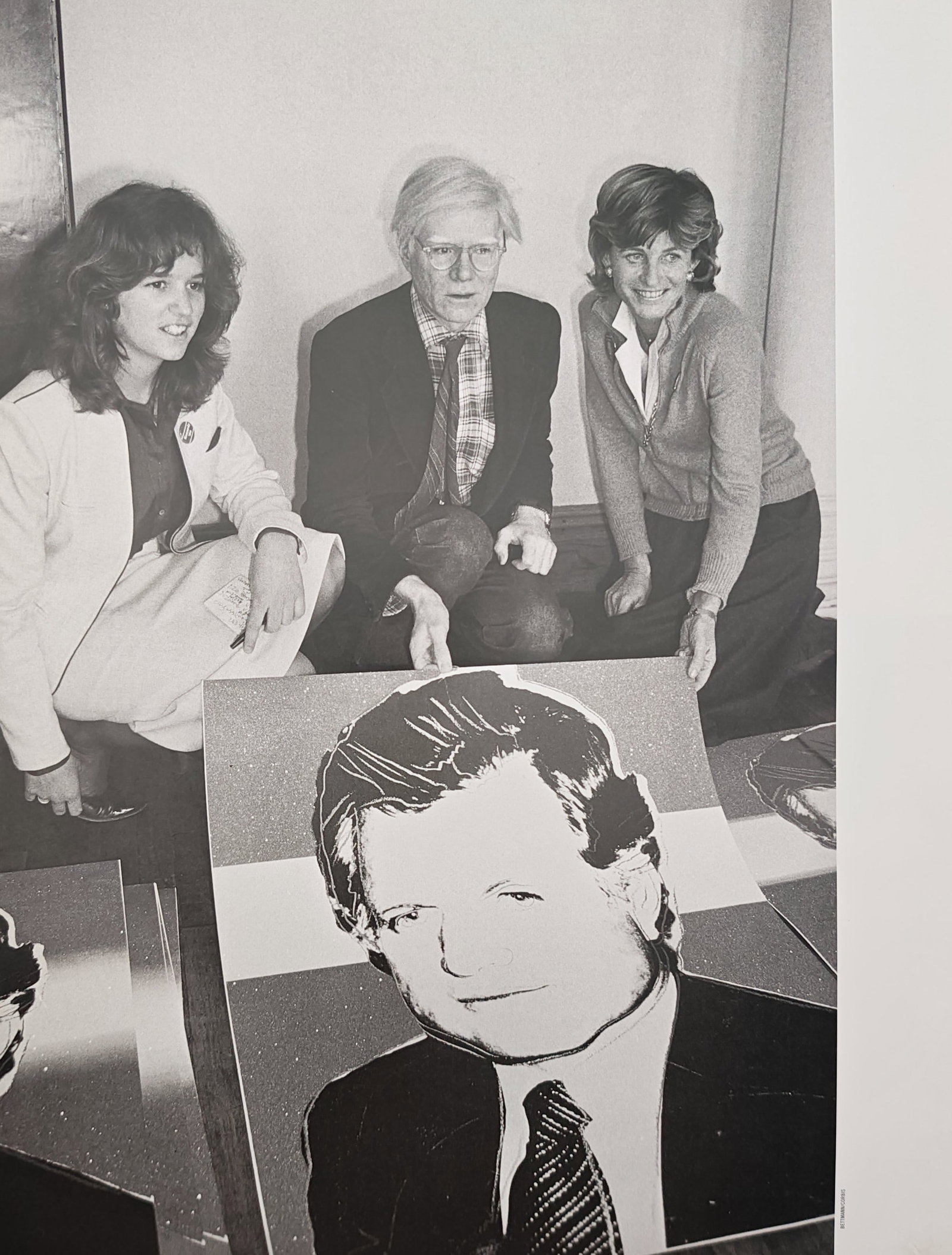 Andy Warhol,after – Ted Kennedy Screenprint Presentation – Offset print (20th Century): "Ted Kennedy Screenprint Presentation" captures a black and white scene of three individuals gathered together while presenting a large graphic portrait print. This documentary image emphasizes the in