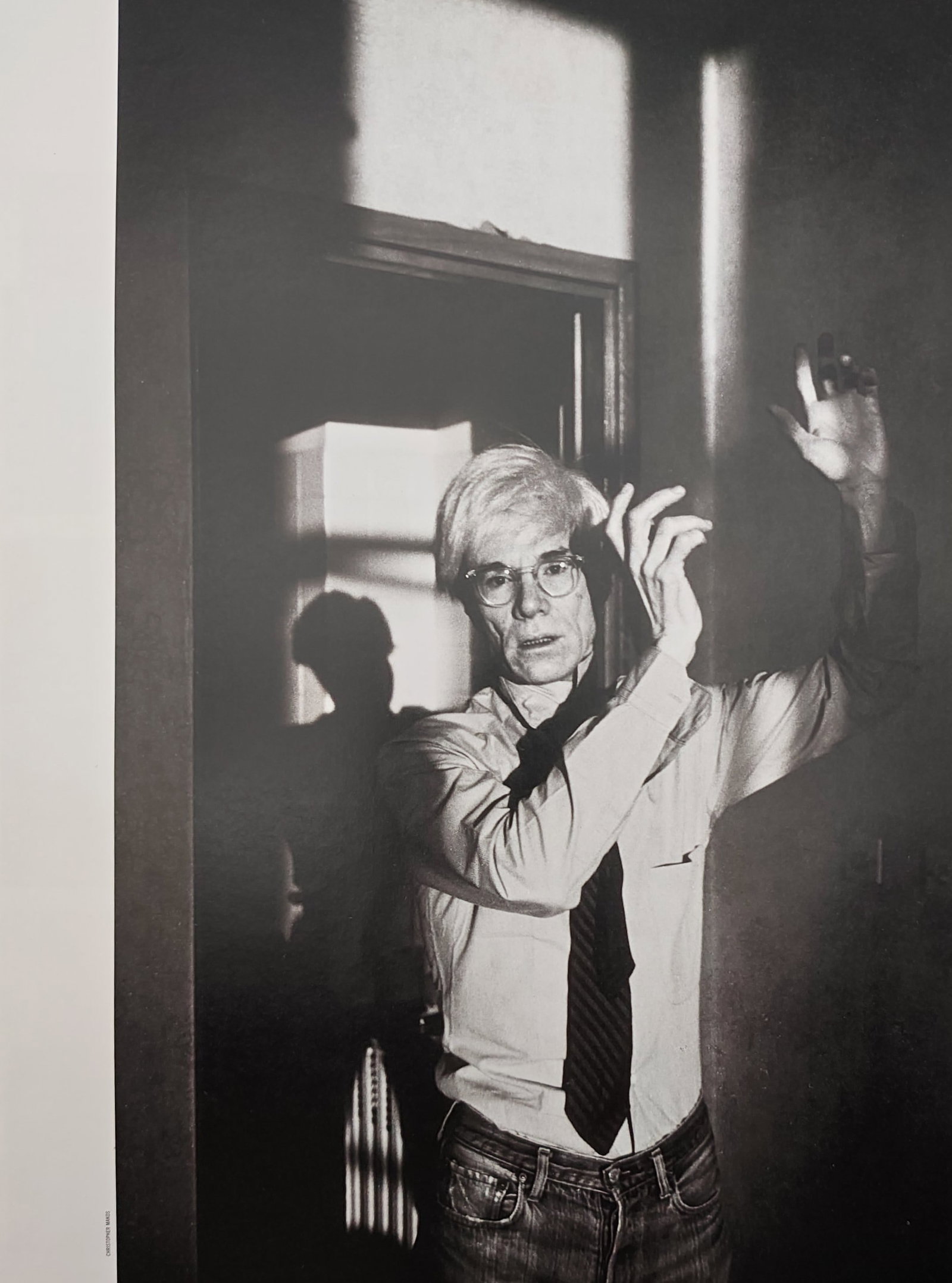 Andy Warhol,after – Self-Portrait with Raised Hands – Offset print (20th Century): "Self-Portrait with Raised Hands" captures a dramatic black and white image of an individual with glasses standing in a doorway with raised arms under stark, geometric shadows. This atmospheric photog