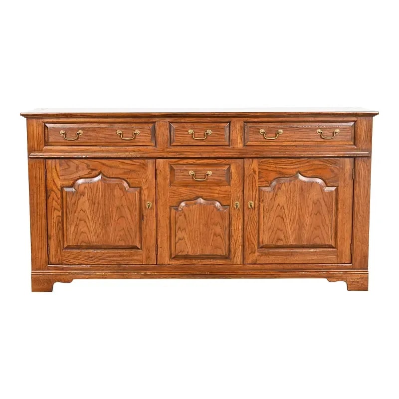 Baker Furniture Welsh Oak Sideboard Buffet or Bar Cabinet: A beautiful Welsh, English Traditional, or Georgian sideboard, buffet server, or bar cabinet By Baker Furniture USA, Circa 1970s Carved oak, with original brass hardware. Measures: 68"W x 19"D x 35"H.