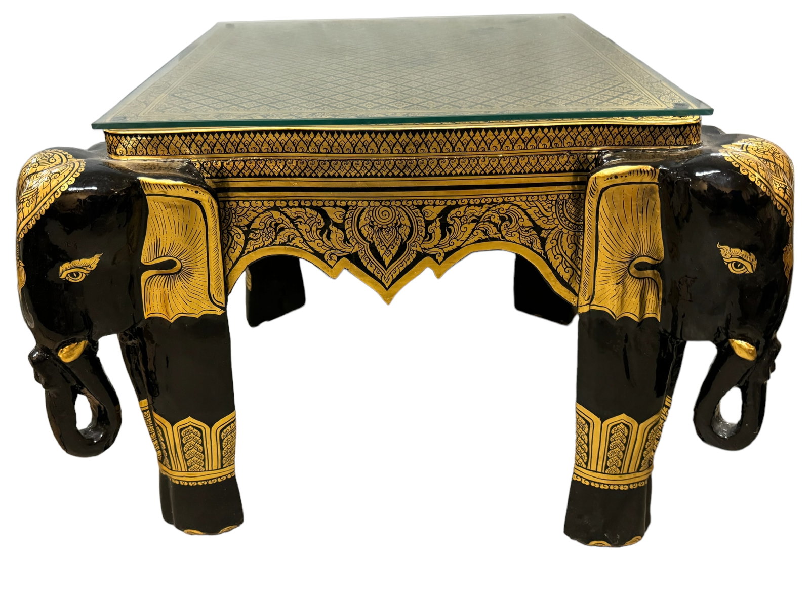 Black Lacquered and Gilded Elephant Side Table: Thai style black lacquered wood side table with figural elephant head legs and intricate geometric gilt paint. Glass topper. Table measures 18.75 x 25 x 25 inches. *** This item requires IN PERSON PIC