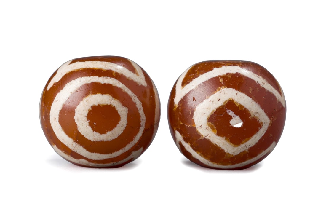 Pair of Tibetan Himalayan Carnelian Agate Eye Bead Amulets: This pair of traditional Tibetan-Nepalese amulet beads is made from carnelian agate, each featuring an eye-like pattern. The beads are believed to offer protection and spiritual strength. Each bead