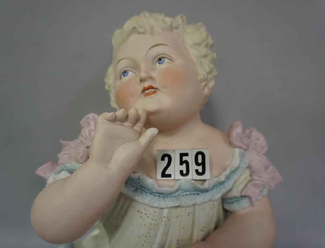 LARGE PAINTED BISQUE PIANO BABY (CONTRA & BOEHME),: LARGE PAINTED BISQUE PIANO BABY (CONTRA & BOEHME), APPROX. 13 IN. H, BASE IS 9 1/4 IN. W AT THE WIDEST POINT, BABY IS IN SITTING POSITION WITH HEAD TILTED UPWARDS, DRESS WITH PINK MOLDED BOW AT EACH S