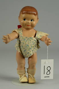 CAMEO GIGGLES DOLL 12 1/2 IN.: CIRCA 1930, ALL COMPOSITION WITH SOCKET HEAD, MOLDED BACK CURL WITH RED TIED RIBBON BOW, BLUE PAINTED EYES, CHUBBY JOINTED FIVE PIECE BODY, FLORAL PRINTED COTTON PLAY SUIT, WHITE CANVAS SHOES, WHITE S