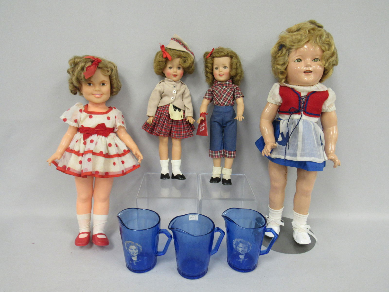 4 SHIRLEY TEMPLE DOLLS & 3 PITCHERS:: (2) 12 IN. ST. OUTFITS "PEDAL PUSHERS WITH PURSE," - "WEE WILLIE WINKLE" (TAGGED ST) 1959 16 IN. ORIGINAL DRESS 1972, 18 IN. IN NEW "BLUE BIRD" OUTFIT, NEEDS TO BE RESTRUNG, EYES CLOUDY, CRAZING OF FA