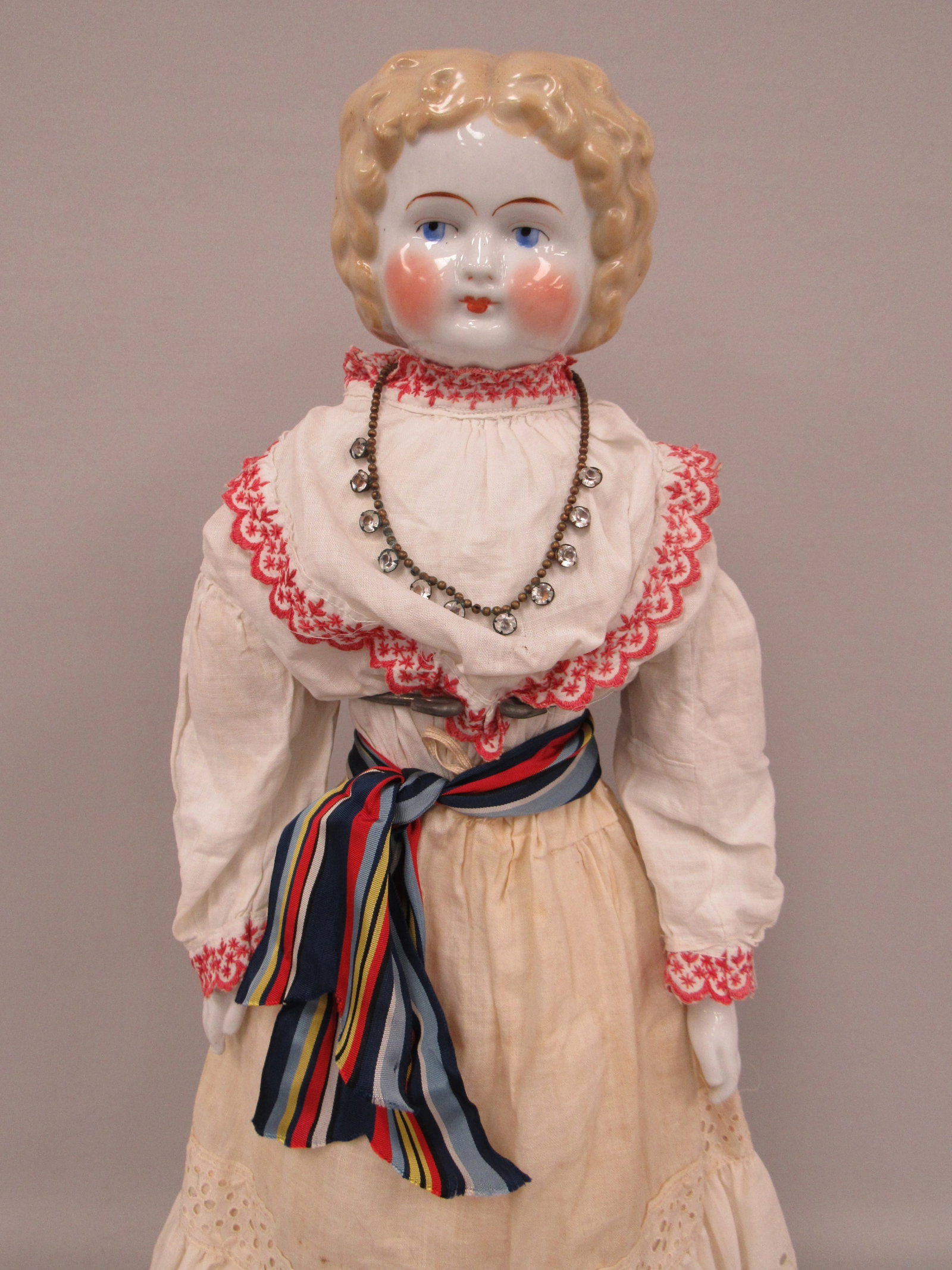 23 IN. CHINA HEAD BLONDE MARKED ON PLATE:: PAT DC 7/80. HEAVY BODY. CHINA ARMS & LEGS. PINK TINT LOWER LEGS WITH STRIPES TO LOOK LIKE STOCKINGS WITH BLUE BOOTS