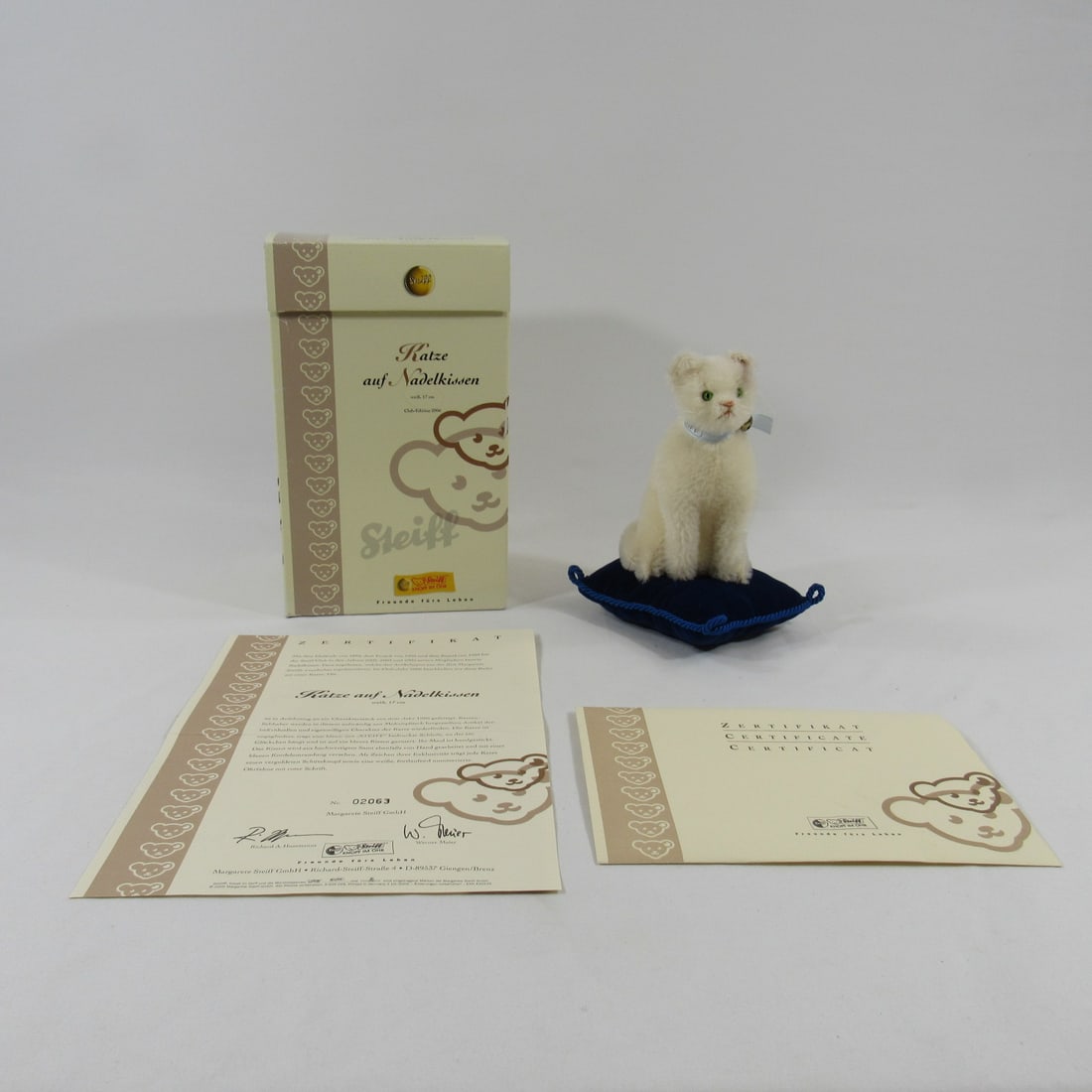 STEIFF CAT ON A PINCUSHION:: 8 IN. H WHITE MOHAIR CAT WITH BLUE RIBBON & BELL. 2006 CLUB EDITION WITH BUTTON & FLAG IN EAR, #02063. C.O.A. INCLUDED & WITH THE ORIGINAL BOX