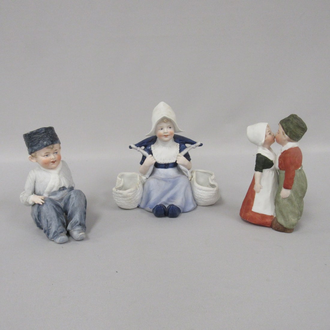 3 HEUBACH FIGURINES:: DUTCH BOY 4.5 IN. H UNMARKED, MISSING RIGHT HAND PINKIE, SMALL FLAKES ON HAT. DUTCH GIRL WITH YOKE & BASKETS, STAMPED NO CHIPS 5 IN. H. DUTCH COUPLE KISSING 5.5 IN. STAMPED, NO CHIPS
