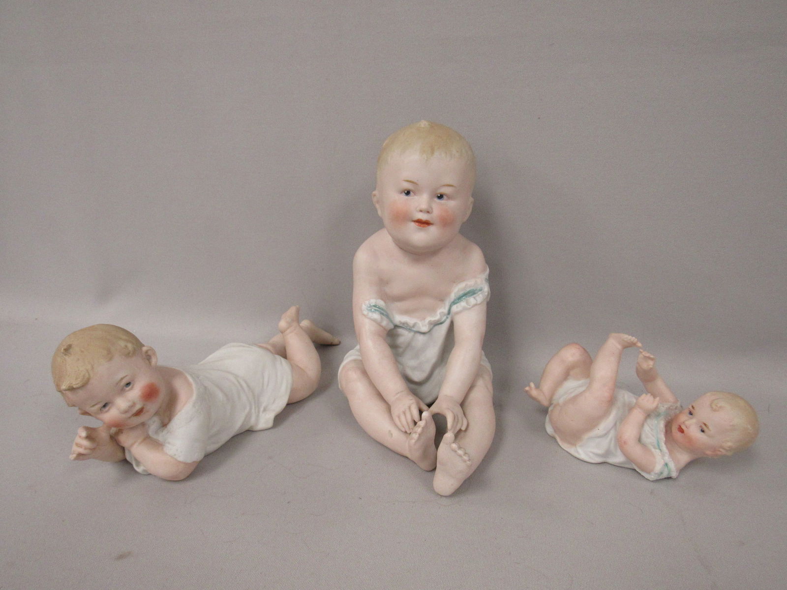 (3) HEUBACH BISQUE PIANO BABIES:: (1) LYING ON BACK - 3 IN. H, 5 1/2 IN. L, 2 IN. W, (1) LYING ON STOMACH - 4 1/2 IN. H, 9 IN. L, 3 1/4 W & (1) SITTING 8 IN. H, 7 1/2 IN. L, 5 IN. W. EACH IS SIGNED WITH HEUBACH "SUNBURST" MARK,