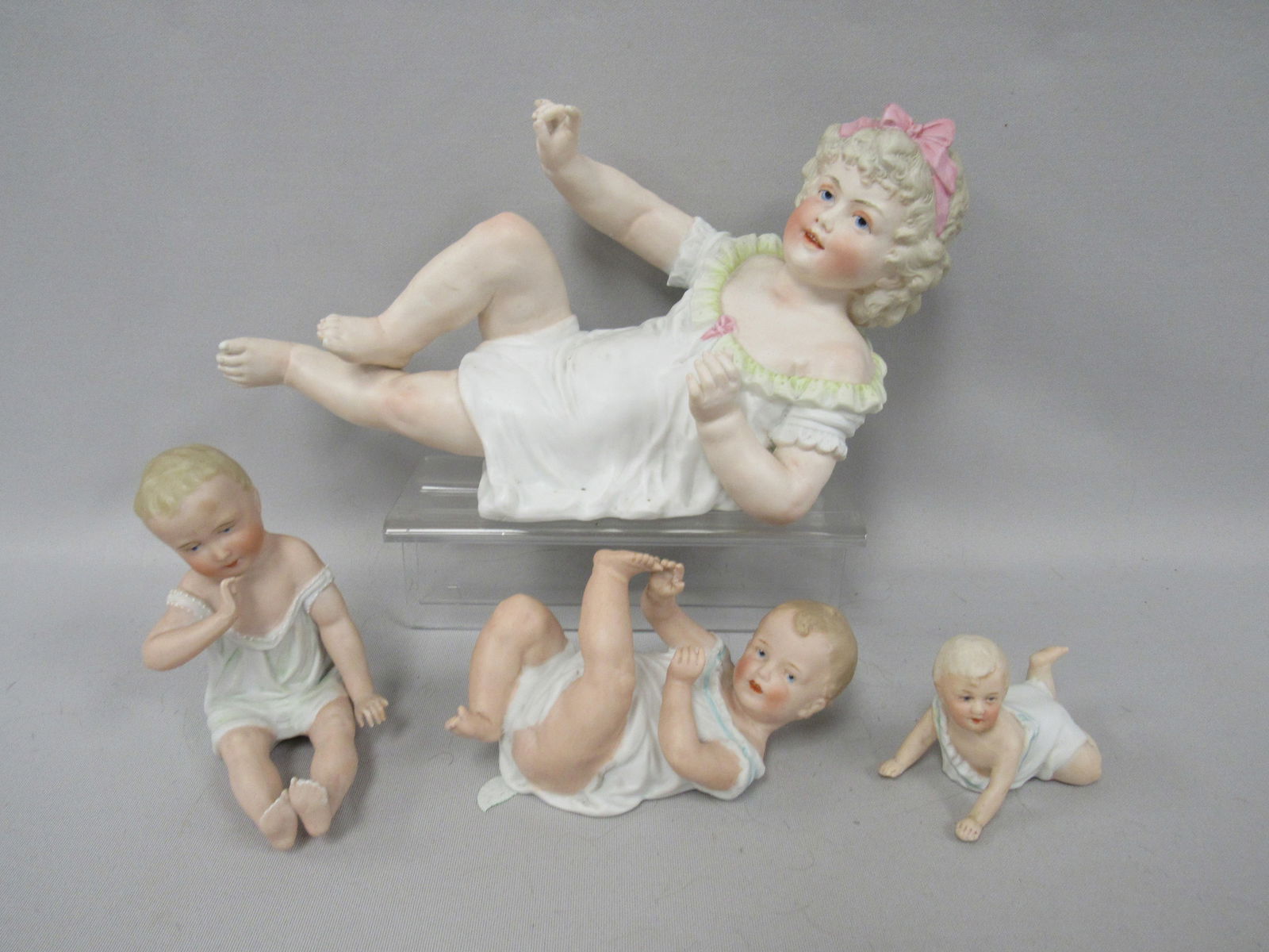 (4) VINTAGE BISQUE PIANO BABIES:: BABY LYING ON BACK IS MARKED HEUBACH 3 IN. H, 5 1/2 IN. L, 2 1/2 IN. W, THE FOLLOWING ARE MARKED: GIRL RESTING ON HER LEFT ARM (459) 6 IN. H, 10 IN. L, 4 1/2 IN. W, BABY CRAWLING 2 1/2 IN. H, 3