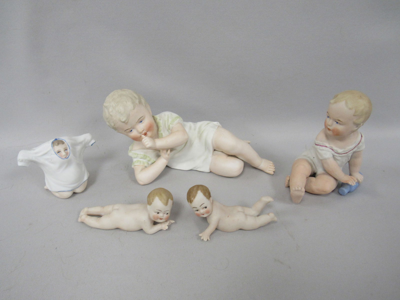 (5) ASSORTED SIZE BISQUE PIANO BABIES:: 1 1/2 IN. TO 5 IN. H, 3 1/2 IN. TO 7 1/2 IN. L & 2 IN. W TO 4 IN. W. 3 PCS. ARE MARKED GERMANY. ONE CRAWLING BABY HAS A SMALL FLAKE ON TOE AREA OF RIGHT FOOT. OTHERS ARE FREE OF DAMAGE OR REPAIR