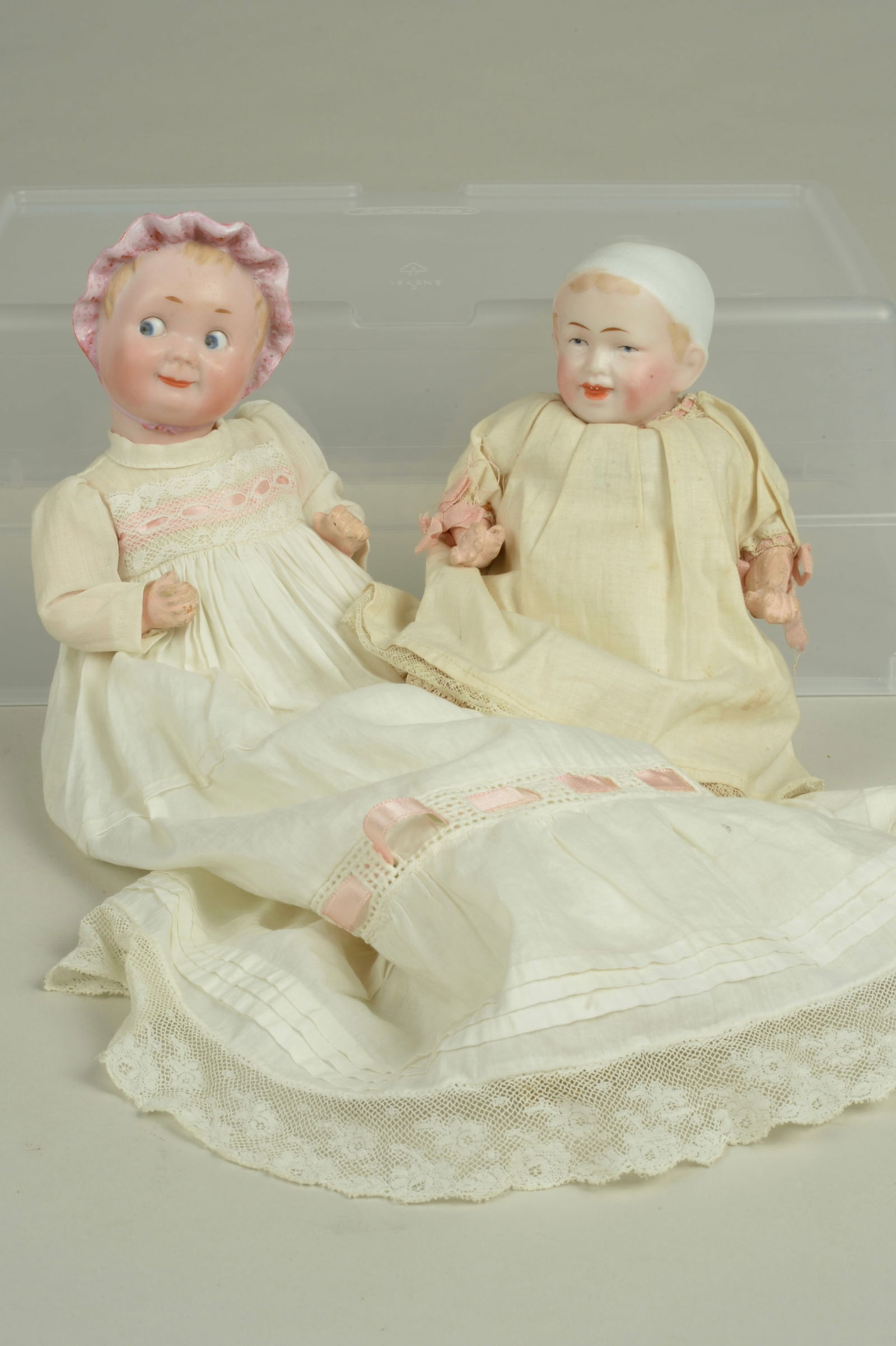 RECKNAGEL CHAR. WITH MOLDED BONNETS 7.5 & 9 IN.:: RECKNAGEL, GERMANY, CIRCA 1920, FINE QUALITY BISQUE SOCKET HEADS, BOTH DOLLS INCISED RA, BOTH HAVE MOLDED & PAINTED FEATURES, SMILING MOUTHS, ON 5 PIECE COMPOSITION BABY BODIES, BOTH HAVE COTTON BABY