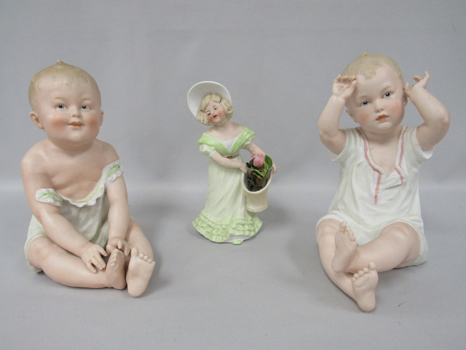 GROUP OF 3 HEUBACH FIGURINES:: FEATURES (2) CLASSIC FIGURES OF BABIES IN SITTING POSITION, 9 IN. H, 4 IN. W, 7 IN. D & 8 IN. H, 5 IN. H, 7 1/2 IN. D. INDEX FINGER (ON BABY WITH GREEN TRIM) ON RIGHT HAND WAS REPAIRED & A HEUBACH