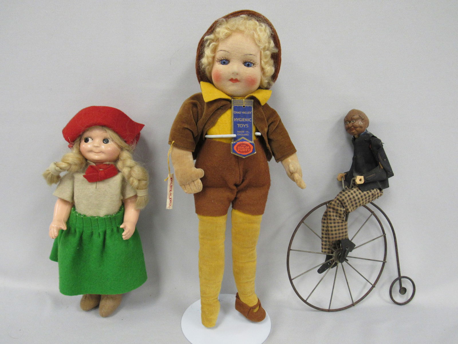 3 PIECE LOT:: PRIMITIVE, CARVED WALNUT HEAD MAN RIDING A VELOCAPEDE (BICYCLE), 10 IN. MADAME HENREDON GIRL COMPO HEAD & ARMS, CLOTH BODY, 14 IN. CLOTH WITH GLASS EYES, CHAD VALLEY WITH TAGS, MISSING A SHOE - G