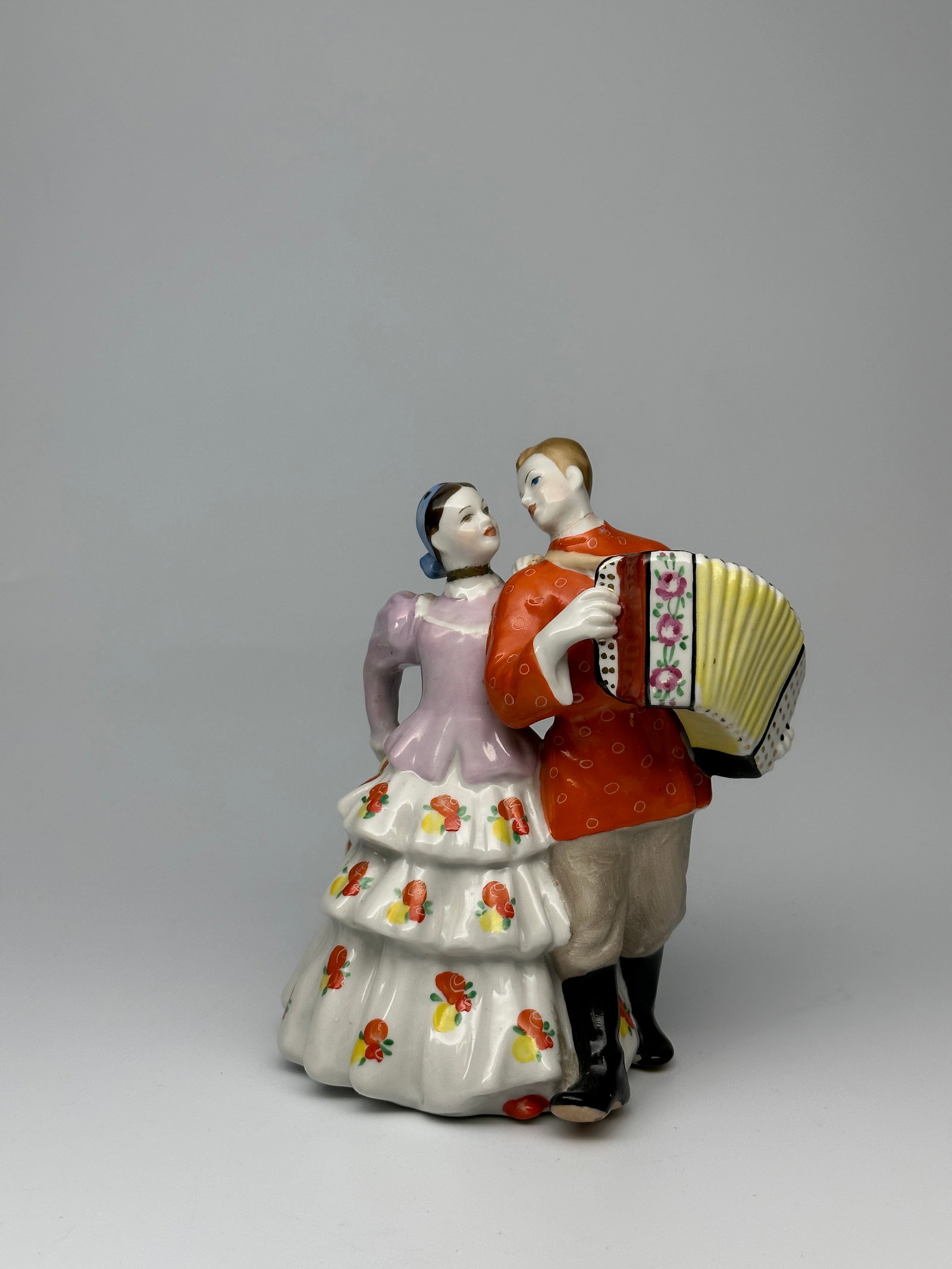 Soviet Porcelain Figurine "Ural Dancing Couple" Dulevo Porcelain Factory: "Ural Dancing Couple" A very fine porcelain figurine depicting a young man and woman dressed in celebratory traditional garments enjoying the evening through song and dance. The man is playing an acco