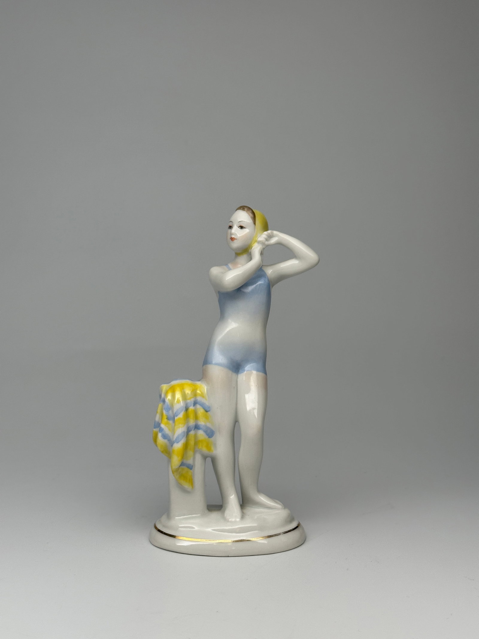 Soviet Porcelain Figurine "Young Swimmer Girl " (Lomonosov Porcelain Factory): Porcelain sculpture of a swimmer girl putting on her swimming cap. Verbilka, Lomonosov Porcelain Factory Produced during 1960s Blue factory makers marks found on underside of base. Height: 6.7 inches