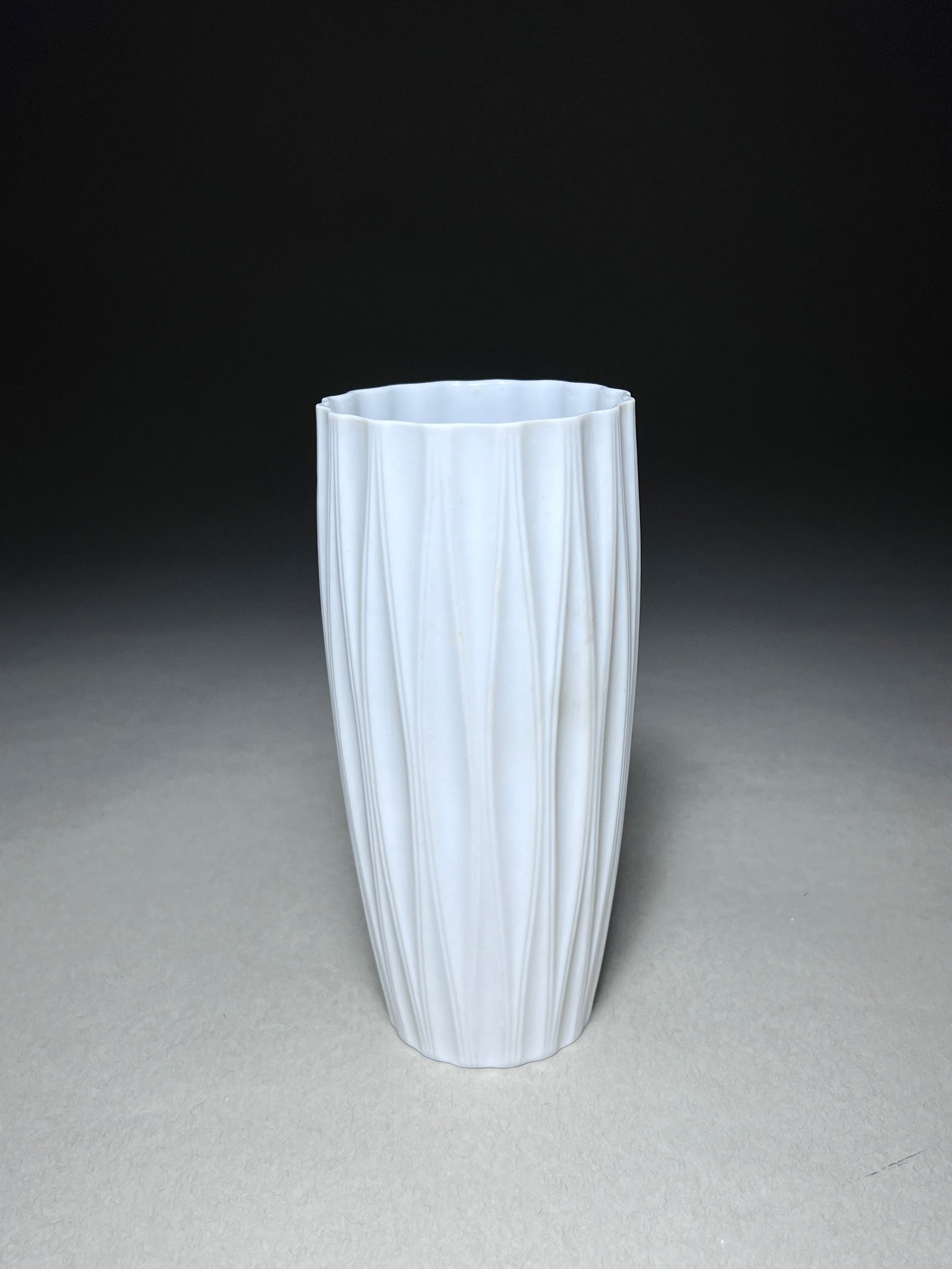 Modernist Fluted White Bisque Vase by Hutschenreuther: The Modernist Fluted White Bisque Vase by Hutschenreuther, crafted in Germany during the 1970s, stands as a striking embodiment of minimalist elegance. Standing at a height of 6.75 inches, the vase ca