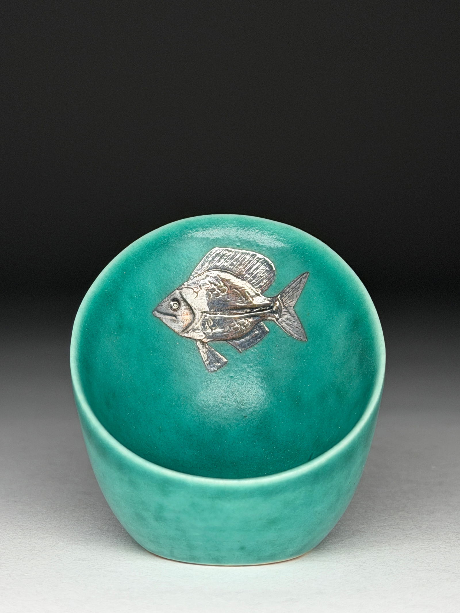 Wilhelm Kage Argenta Stoneware Vessel with Fish Motif: Wilhelm Kage Argenta Stoneware Vessel with Fish Motif A rounded vessel with smooth vertical sides The surface is coated in a luminous turquoise-green glaze characteristic of the Argenta line. At the c