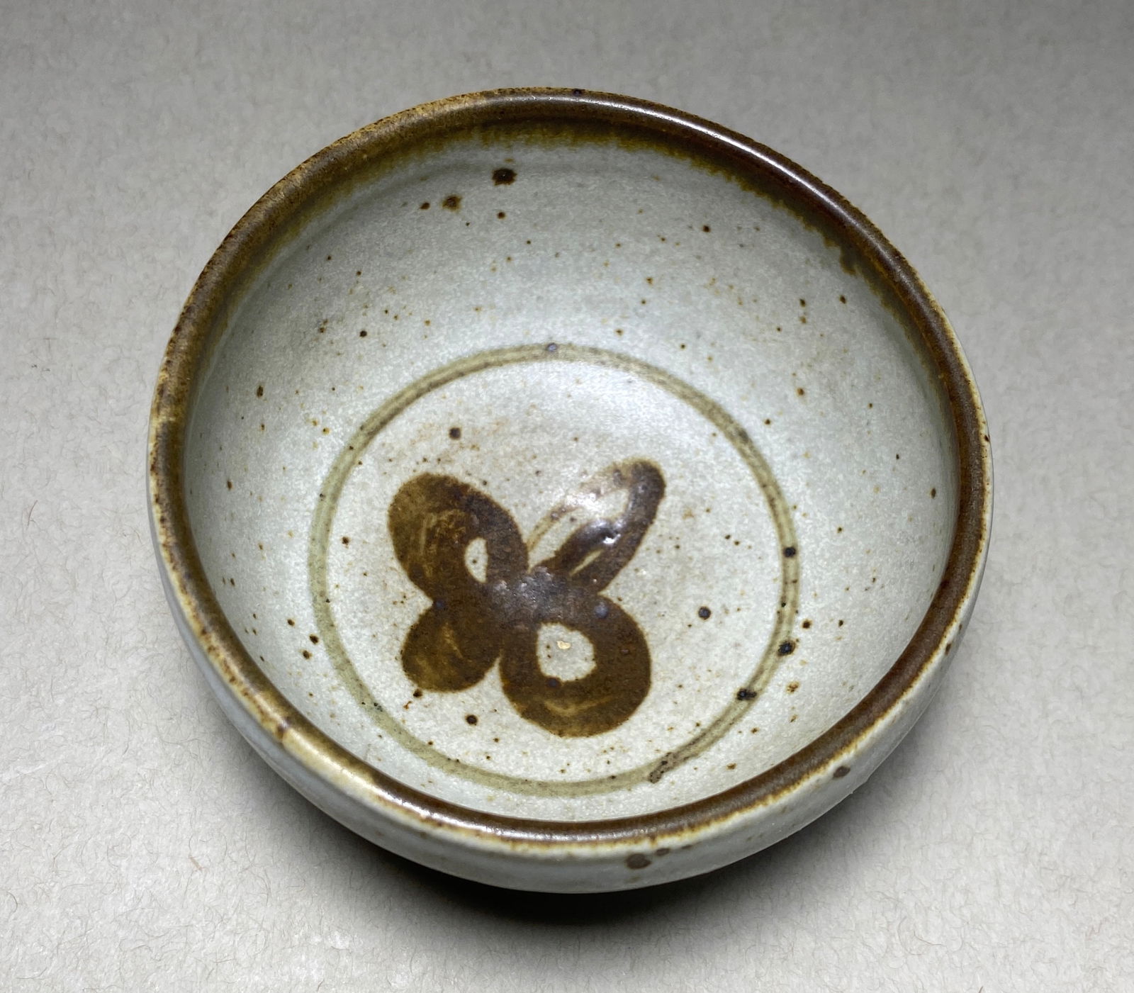 small tan bowlStudio Sake Bowl with Butterfly Motif Mid-20th Century: Studio Sake Bowl with Butterfly Motif Mid-20th Century A stoneware sake bowl featuring a minimalist aesthetic with subtle Asian influences. The piece is distinguished by a delicate iron-oxide butterfl