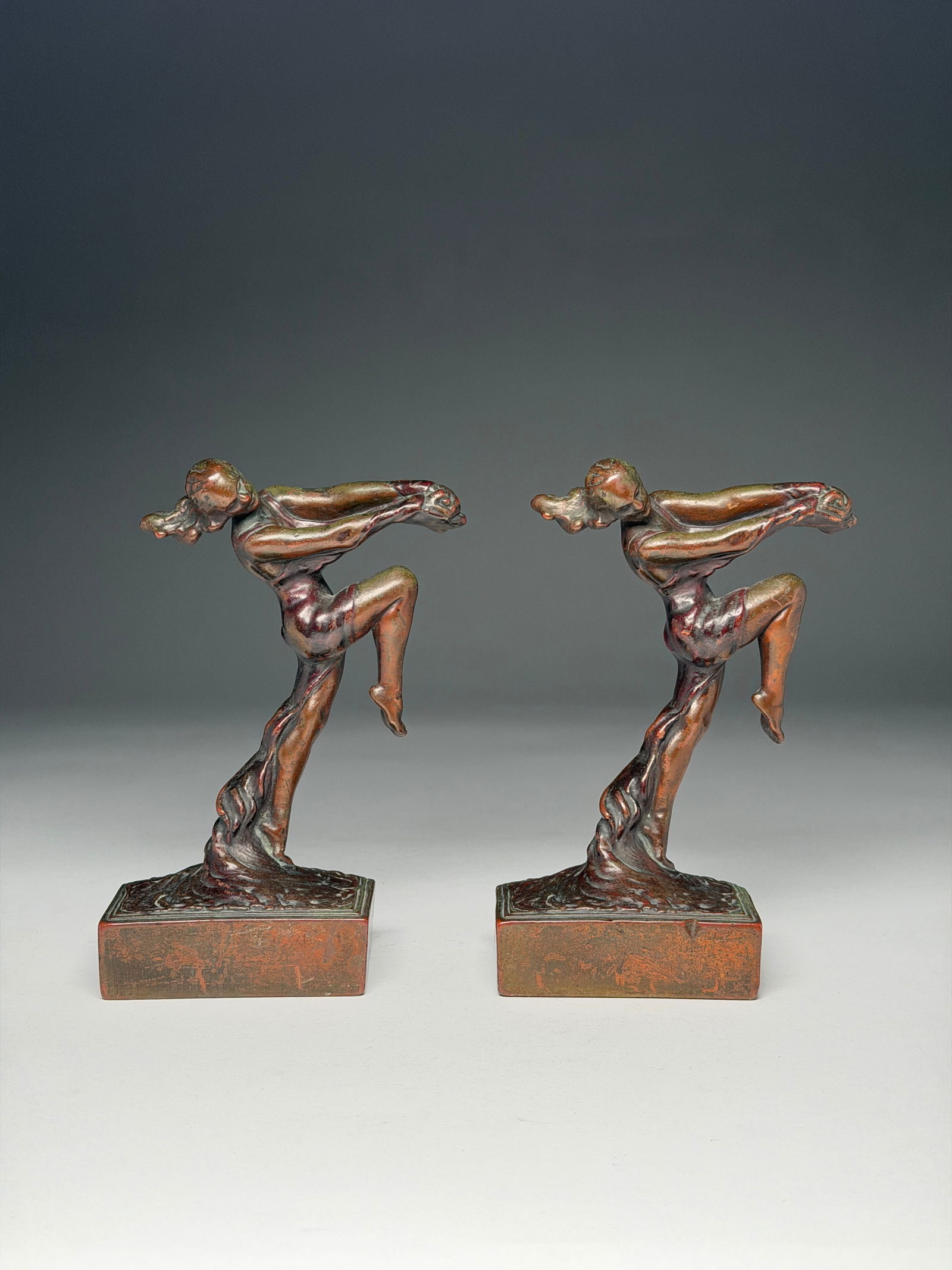 Max Le Verrier Patinated Metal Figural Bookends - Art Deco: Max Le Verrier Patinated Metal Figural Bookends - Art Deco A dynamic pair of sculptural bookends depicting stylized female figures captured in motion, each poised in a forward-leaning stance with one