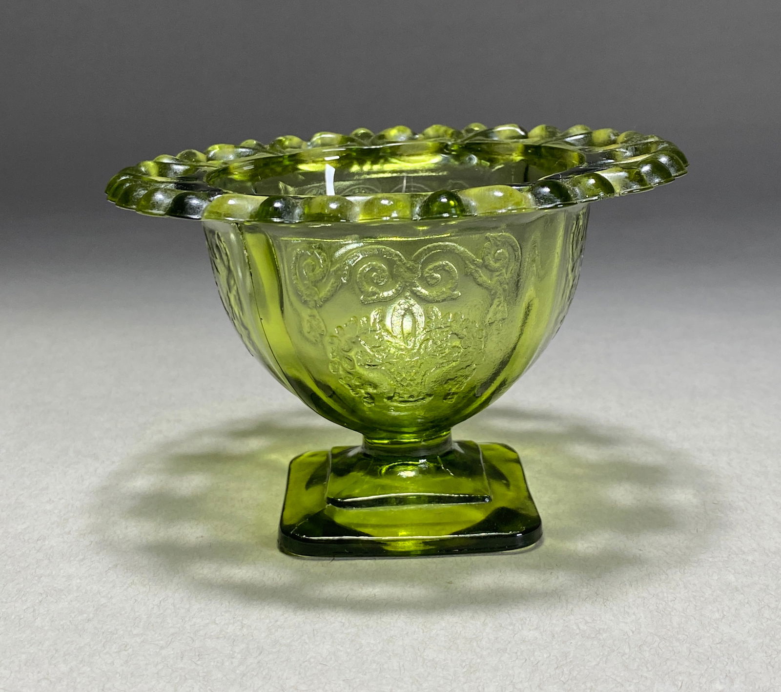 American Pressed Green Glass Compote, Mid-20th Century: American Pressed Green Glass Compote, Mid-20th Century A charming pressed glass compote in vibrant chartreuse, featuring an ornate design with a lace-edged rim and classical floral motifs. The bowl ex