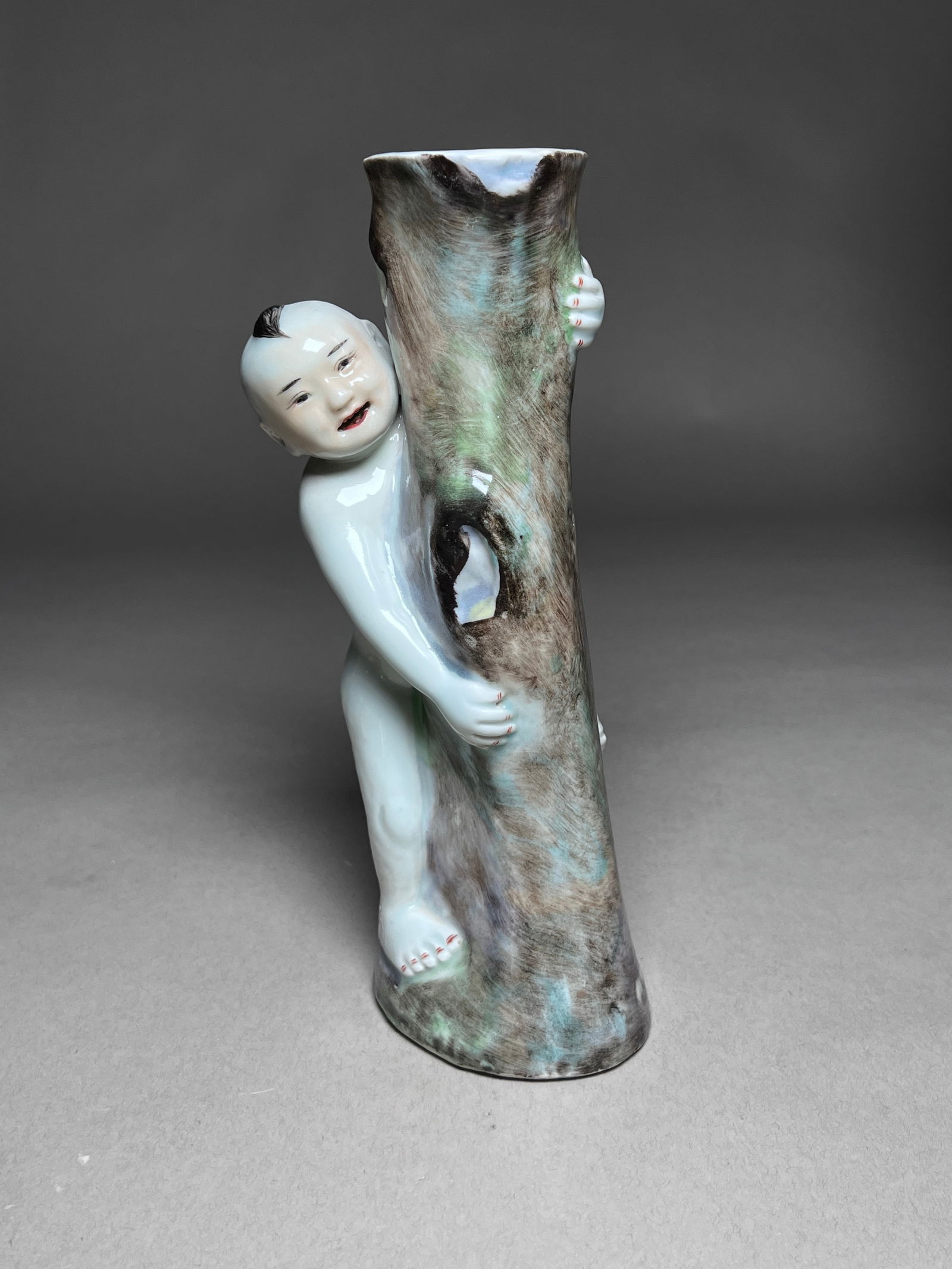 Chinese Export Porcelain Figure of a Child Embracing a Tree Trunk Vase, 19th century: Chinese Export Porcelain Figure of a Child Embracing a Tree Trunk Vase 19th century Modeled porcelain figure features a young boy joyfully leaning against a hollowed tree trunk, which serves as a vase