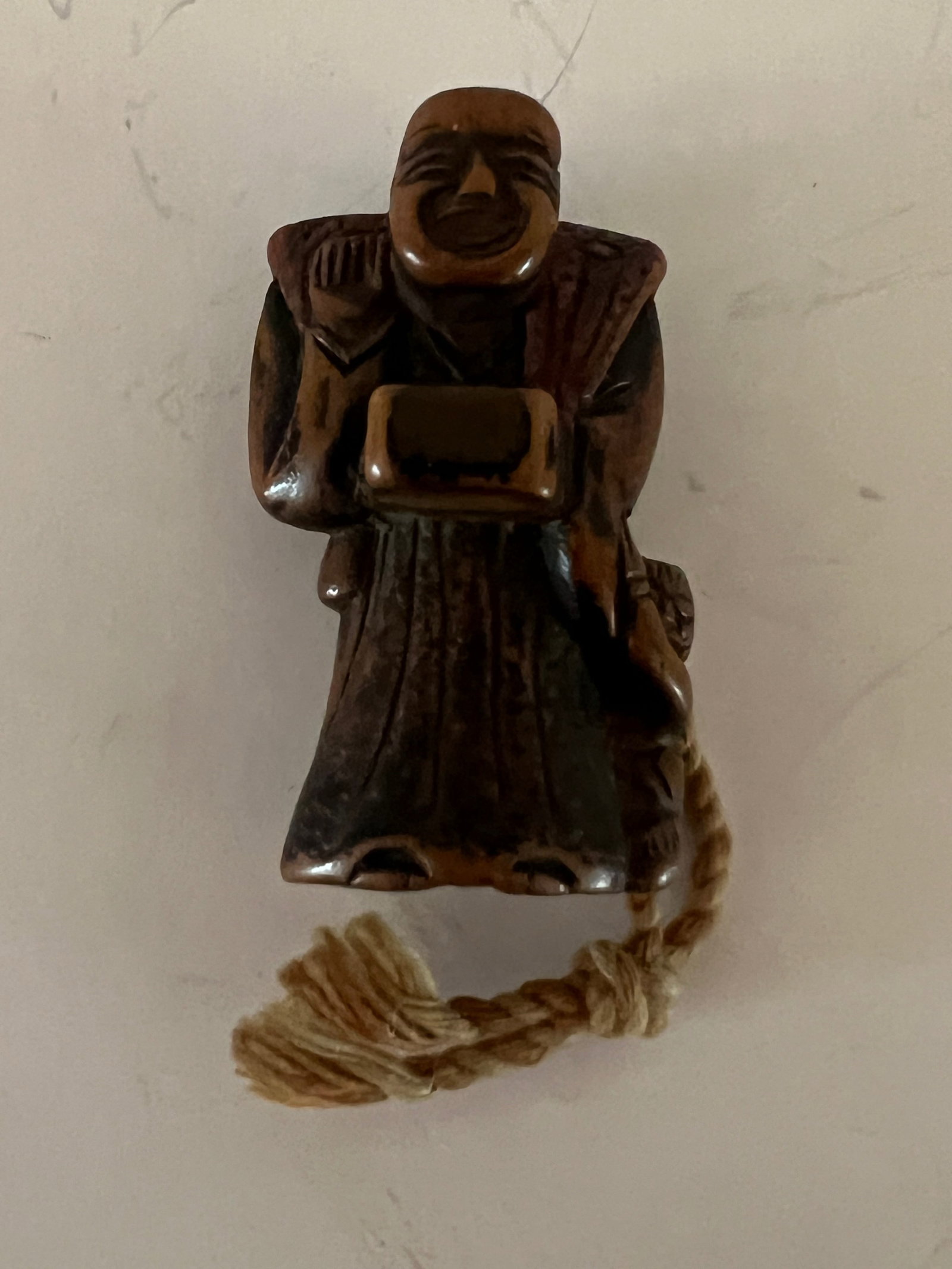 Fruitwood Netsuke of Shinto Priest and Mokugyo, 19th: Patinated Fruitwood netsuke of a Shinto priest cleaning a mokugyo, a fish head-shaped drum used in Buddhisgt rituals that has become a symbol for attentiveness, 19th century. Dimensions: 1 1/2" x 2" x