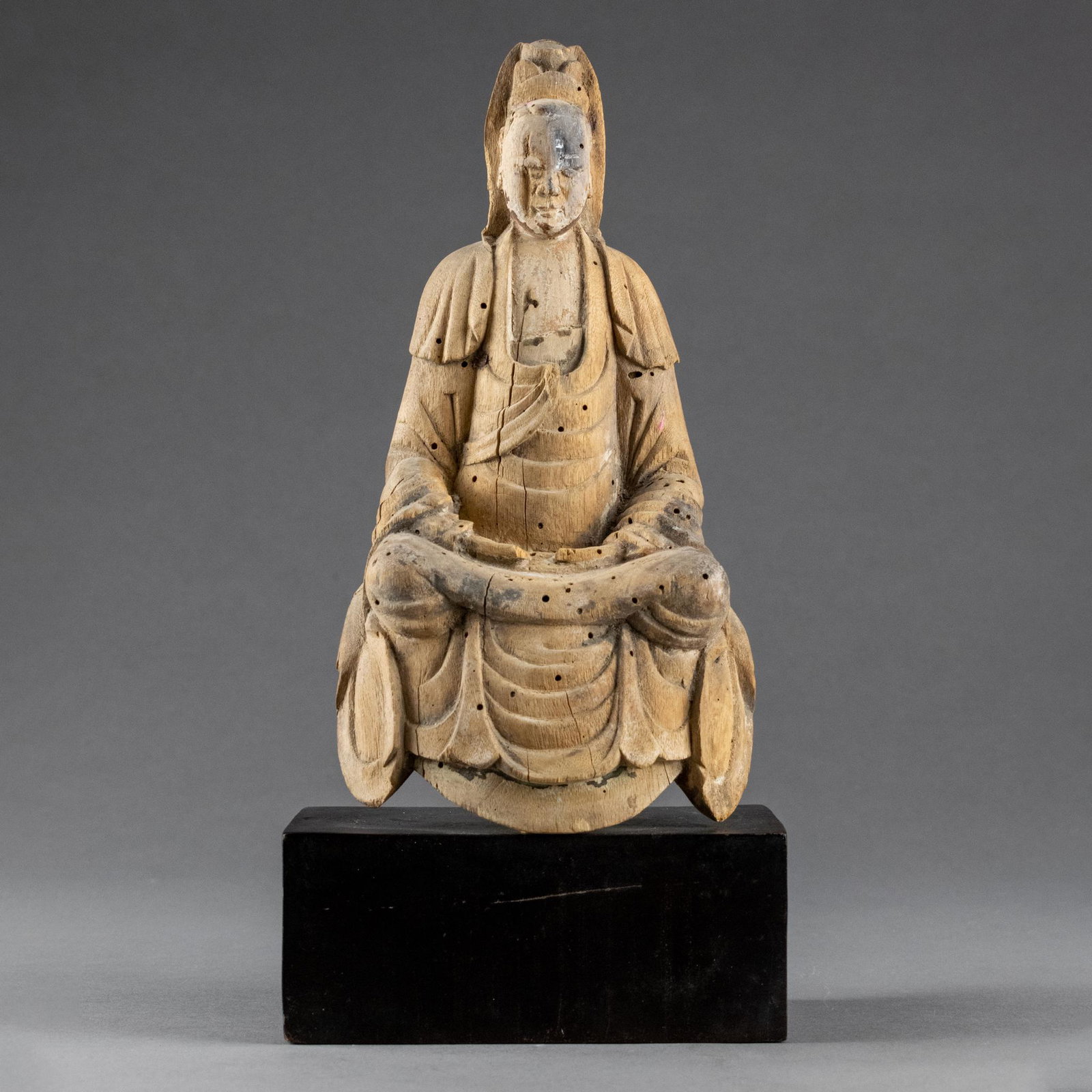 Chinese Carved Wood Seated Guanyin: Ming dynasty or later. Seated in dhyanasana on a raised plinth, the hands held in the lap, the long robes draping in folds over the body and open at the chest, the serene face with a down cast meditat