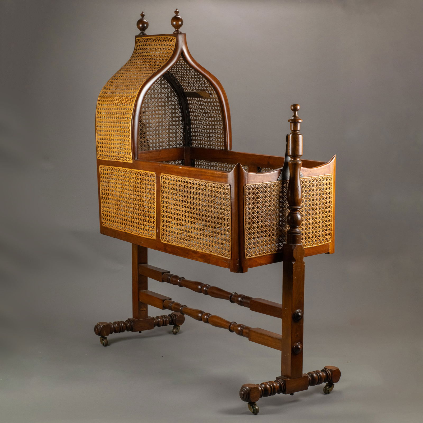 Victorian Cradle: 19th century, the pointed arched caned canopy and base hung between ring turned and square section standard end supports joined by similar double stretchers and splayed feet with castors. For a simila