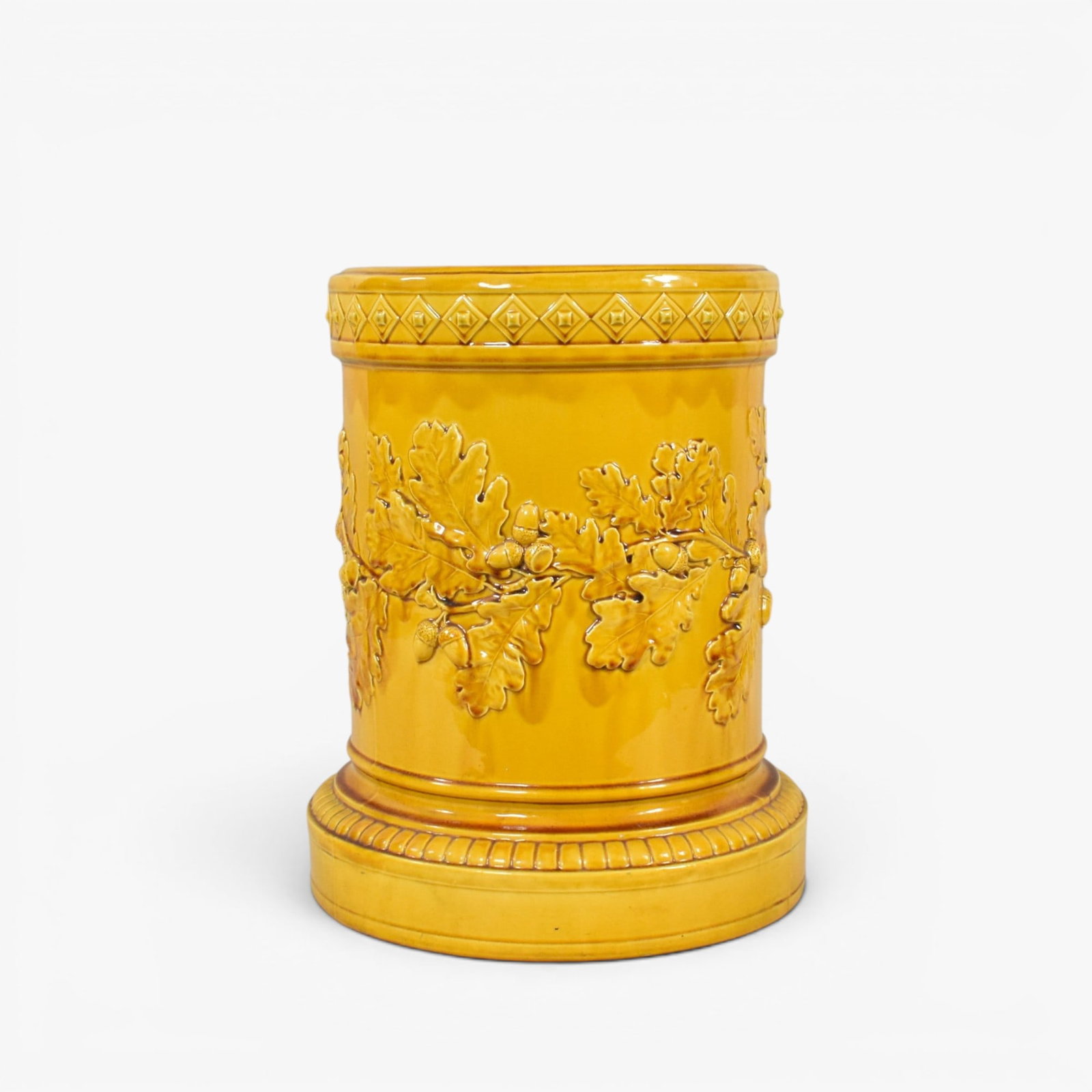 Gold Glazed Majolica Style Stool: 20th century, the cylindrical shape worked in relief around the sides with oak leaves bearing acorns, bordered by line and knop bands, the seat with a stylized, pierced flowerhead, all under a gold gl