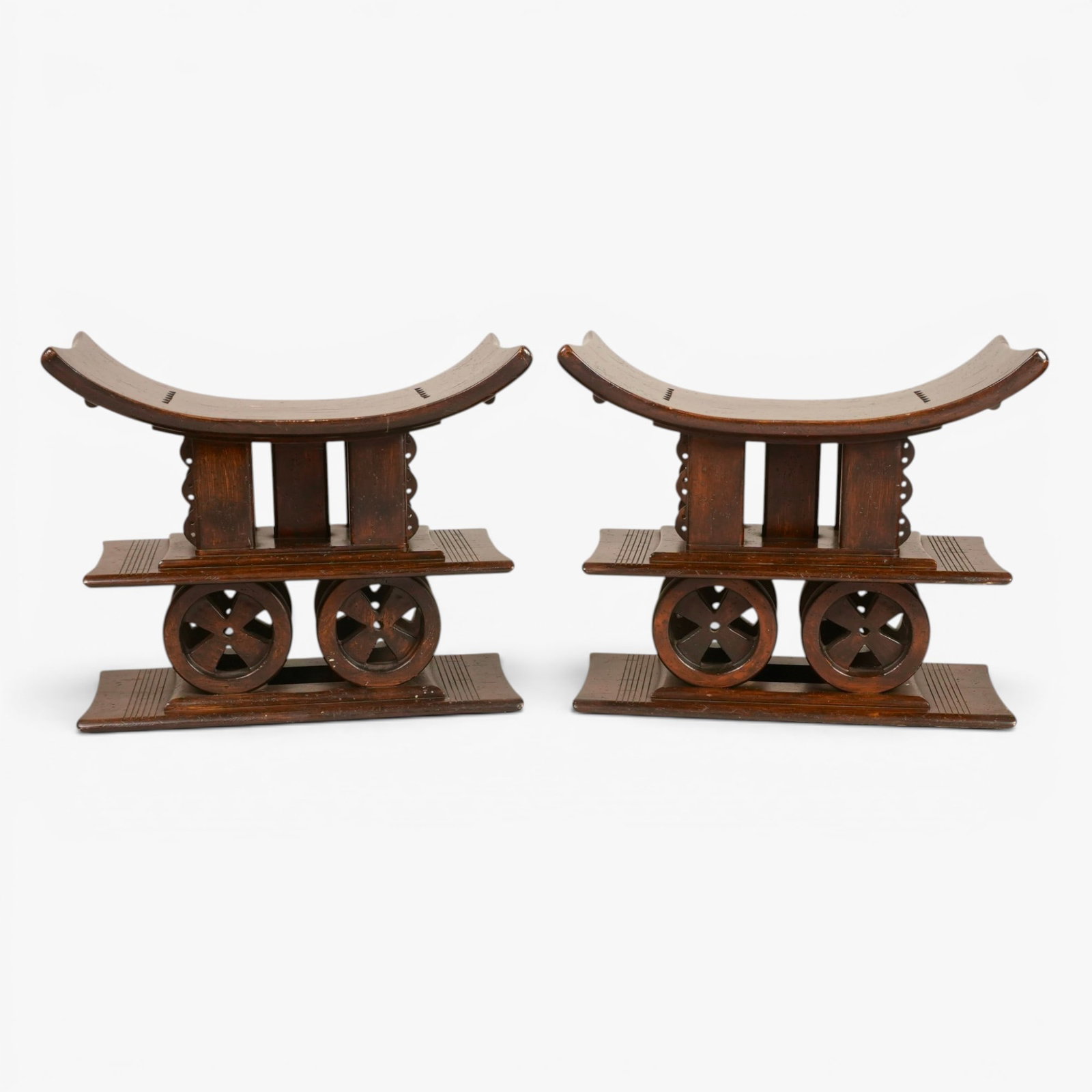 Two African Asante Style Stools: 20th century, Ghana, hand carved, the curving seat supported on five vertical posts, the exterior posts caved with semi-circular flanges, set on a rectangular plinth supported by four circular