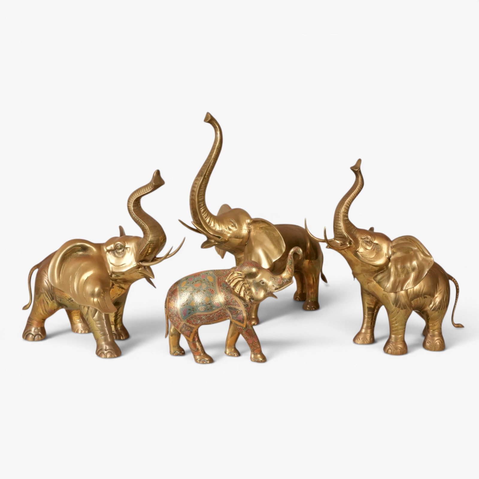 Group of Four Brass elephants: Each in a similar striding pose with the trunk raised, the smallest with incised detailing with blue, red and black coloring The collection of Frank and Irene Giuffrida, owners of the famous Hilltop