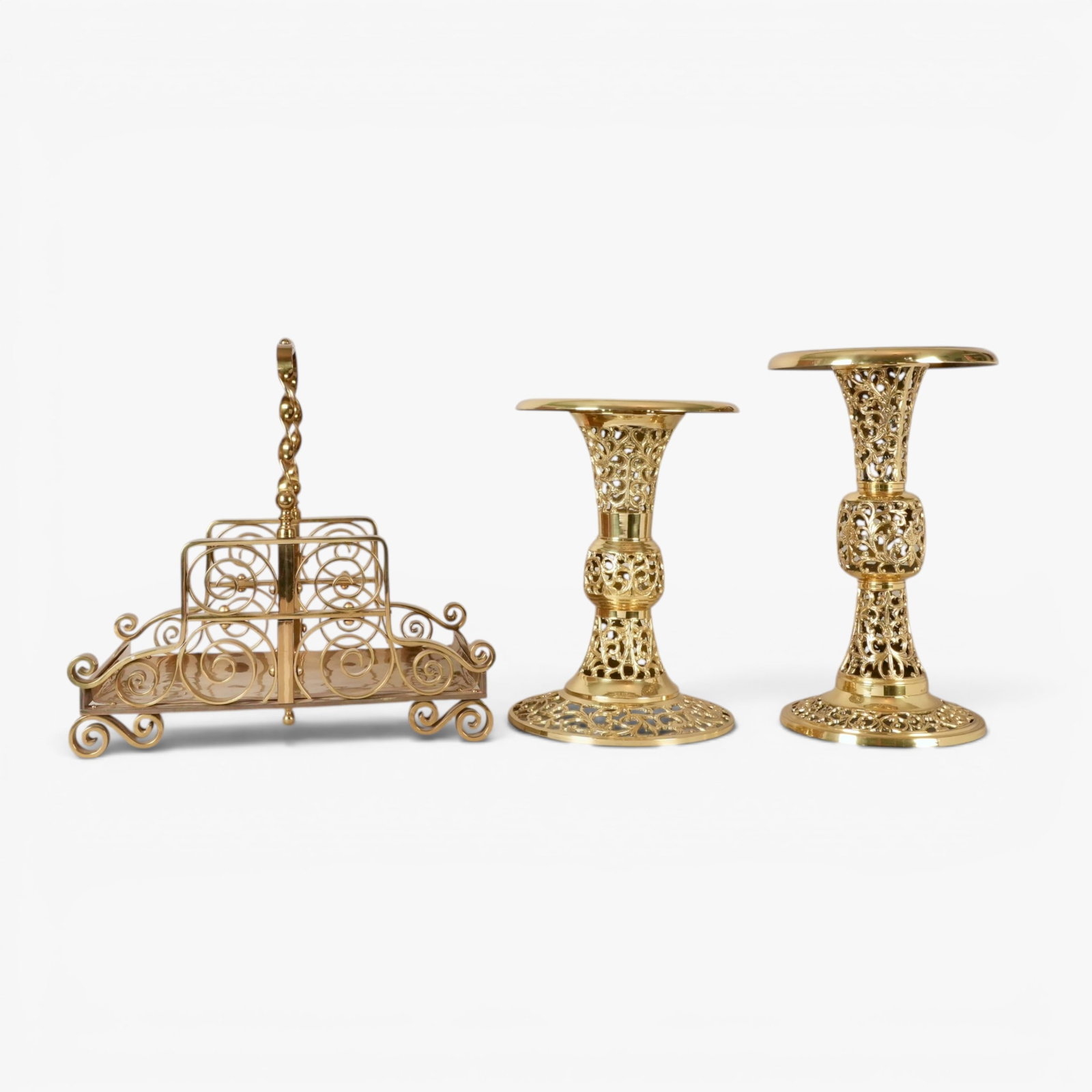Two Brass Pedestals and an Ornate Brass Fireplace Log Holder: Log holder measurements h. 19.5, d. 14, w. 19.5 in; largest pedestal h. 19, d. 11.5 in., smallest pedestal h. 16.5, d. 11.5 in The collection of Frank and Irene Giuffrida, owners of the famous